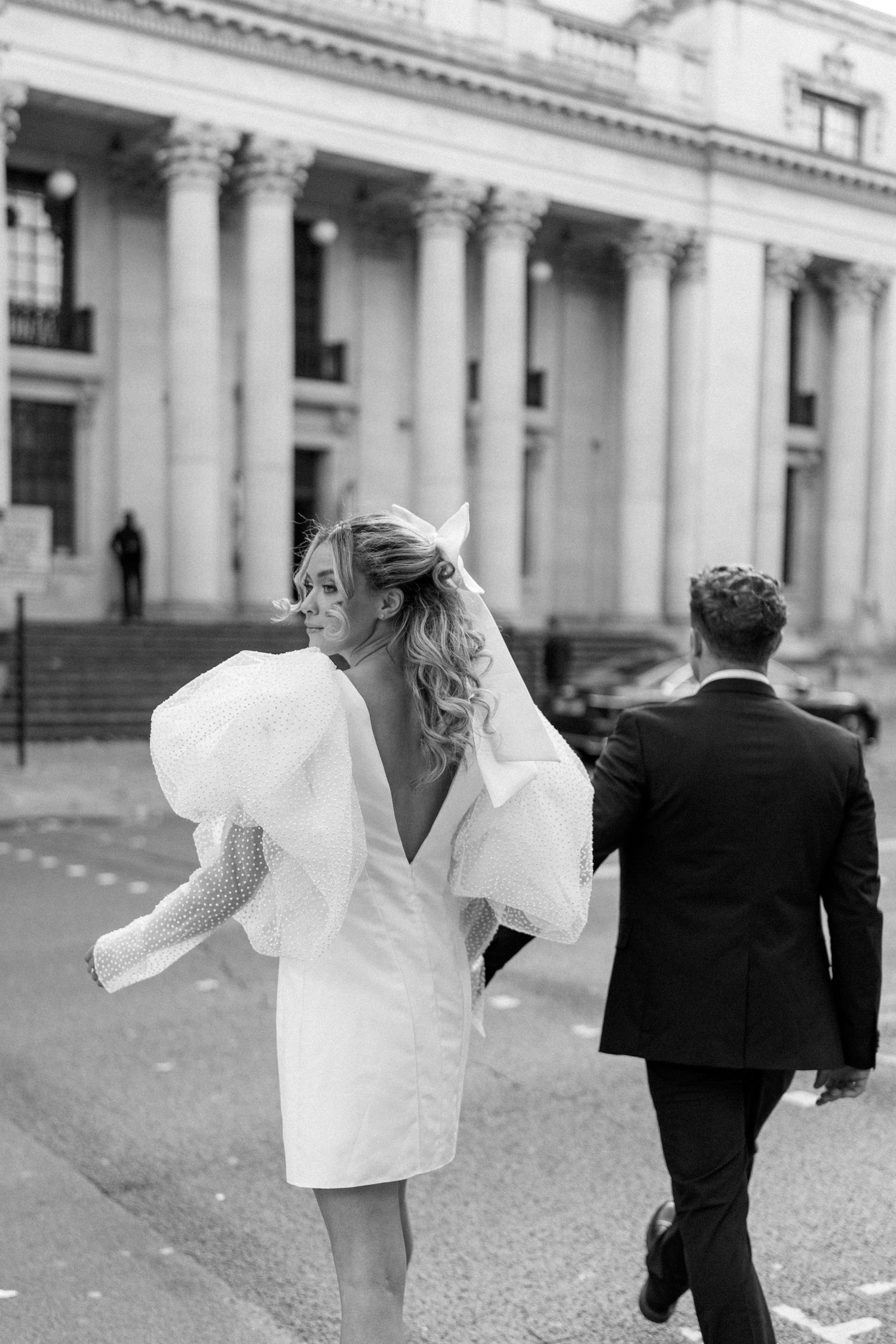 Couple runs playfully through a classical colonnade in black and white photography.