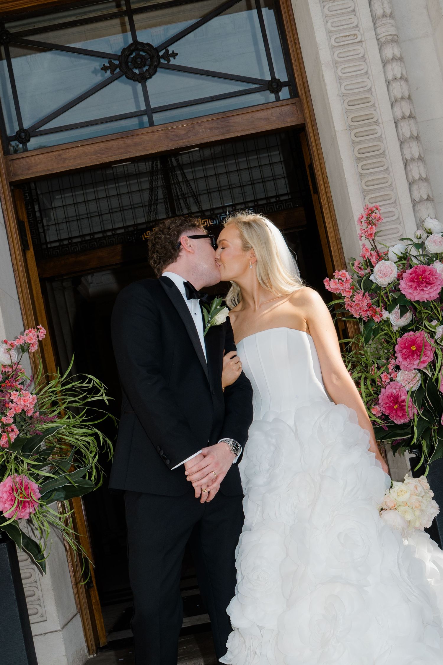 Bride and groom share a kiss in front of floral arrangements at their elegant wedding ceremony.