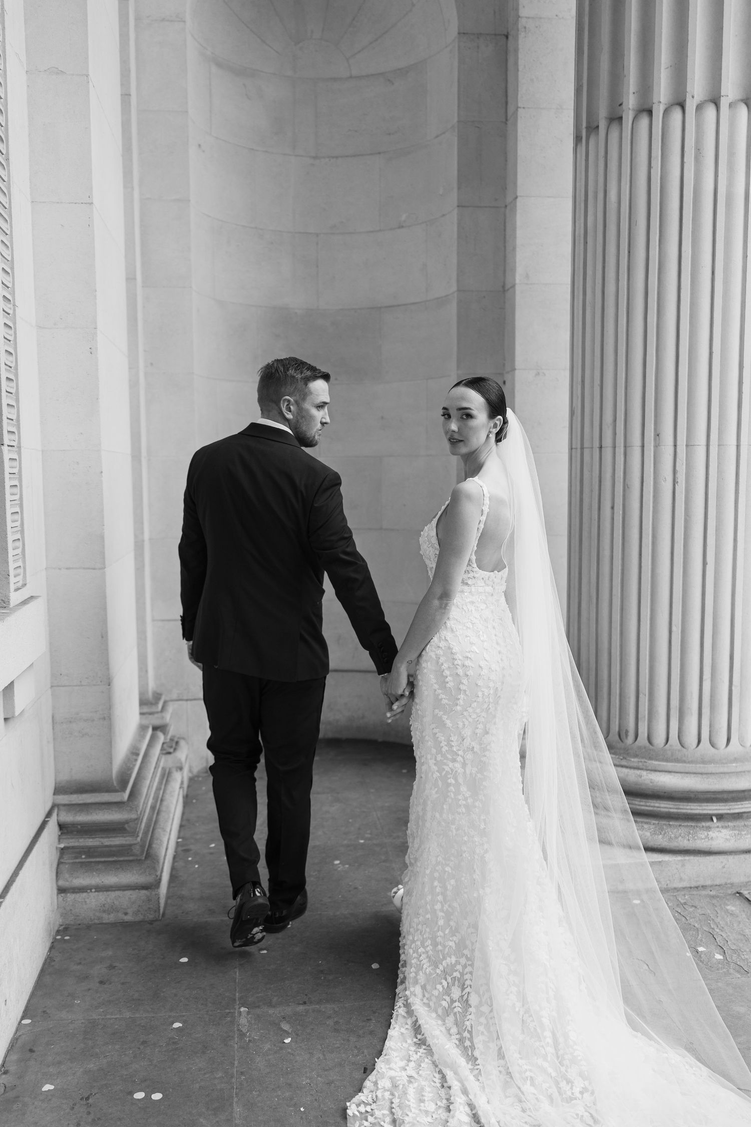 Candid wedding photos of couple walking through an elegant columned gallery.