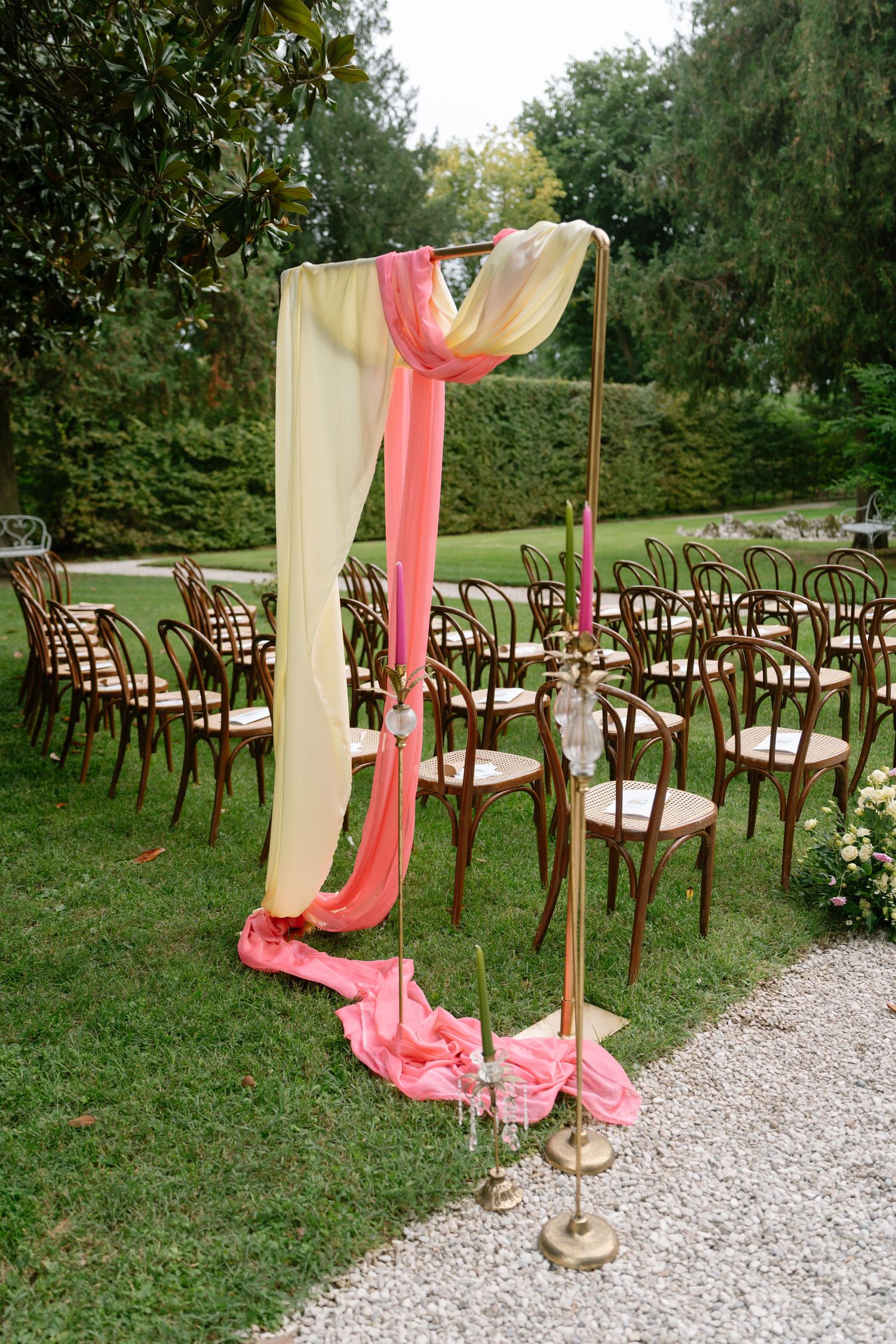 Wedding aisle decorated with coral drapes and wooden poles against a garden backdrop.