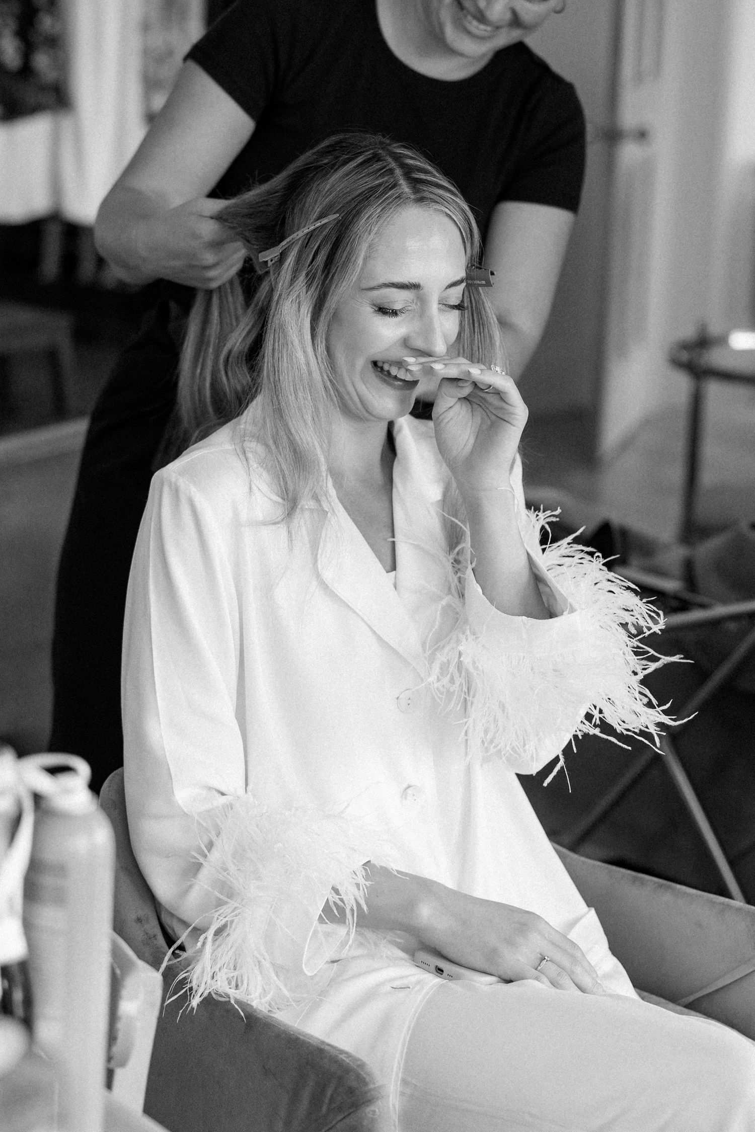 Black and white photo of someone getting their hair styled while wearing a white feathered robe.