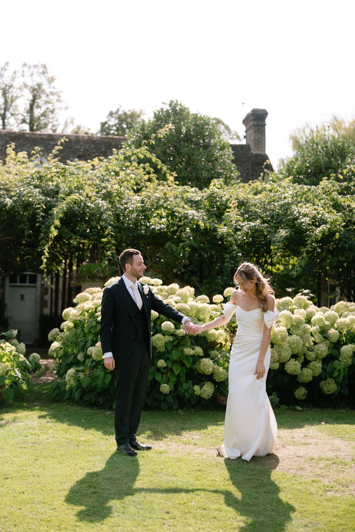 Playful wedding couple dances and twirls among flowering hydrangea bushes.