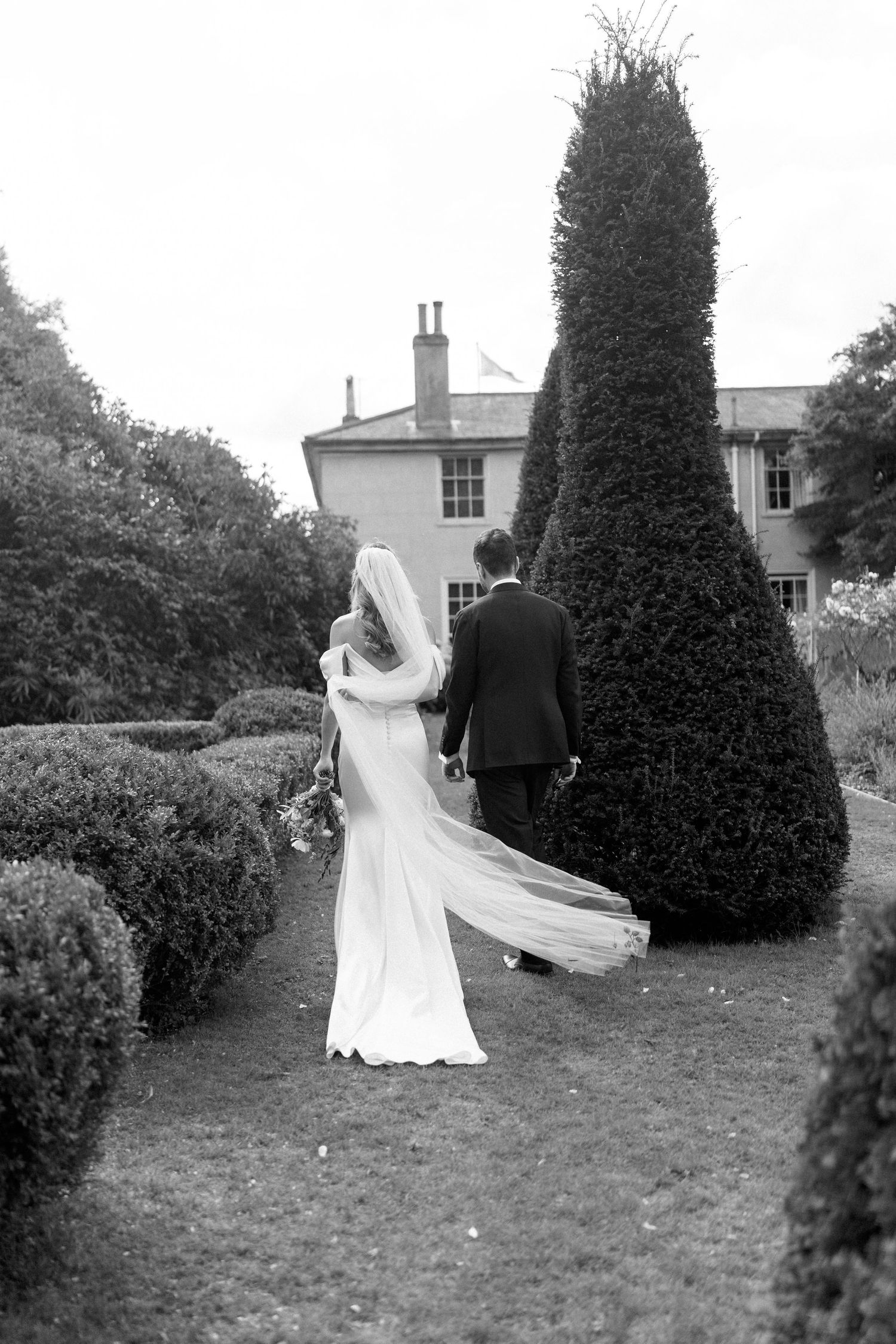Black and white wedding portraits captured in a formal garden with architectural elements.