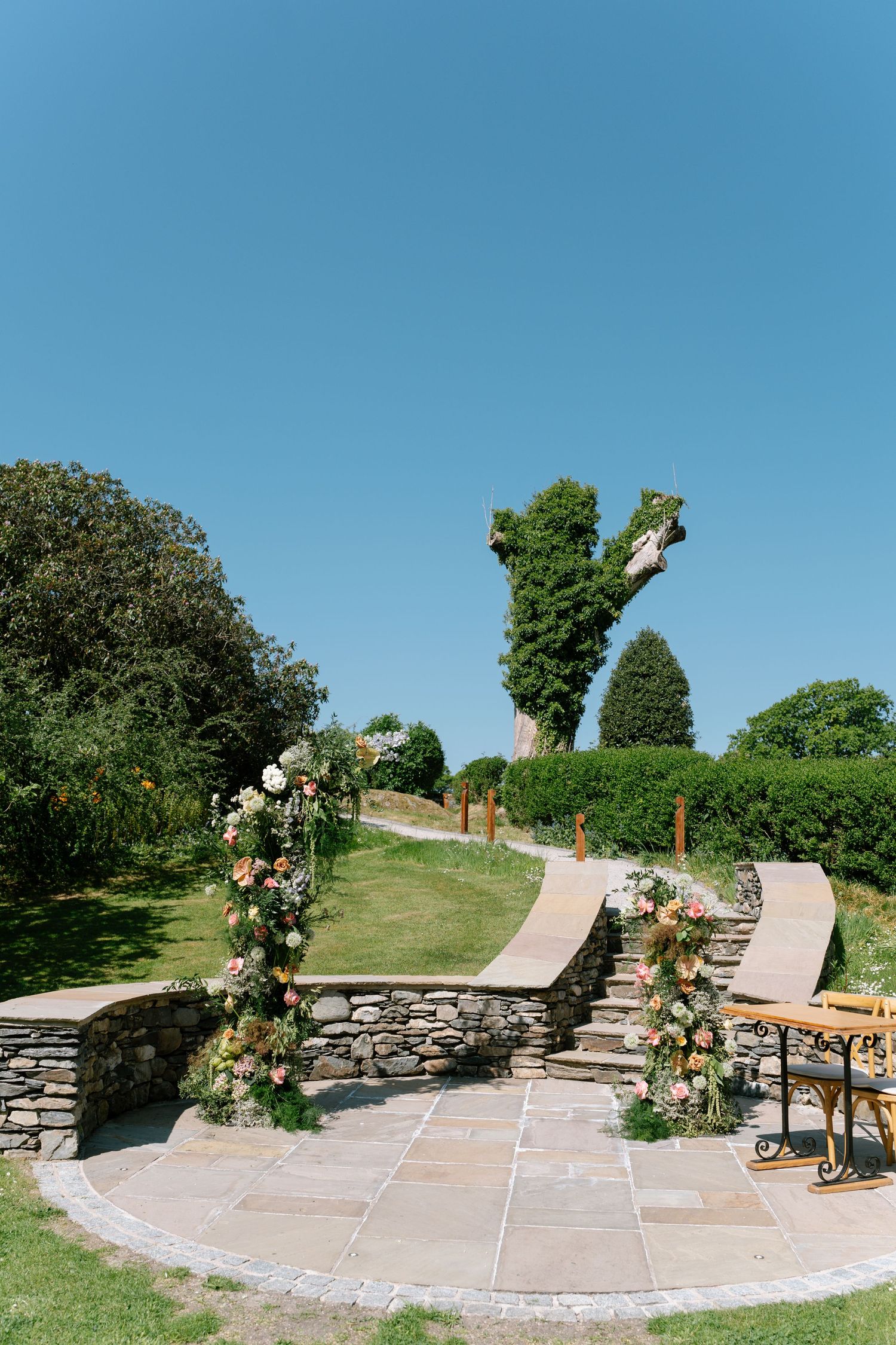 Curved stone pathway with floral arches set up for an outdoor wedding ceremony.