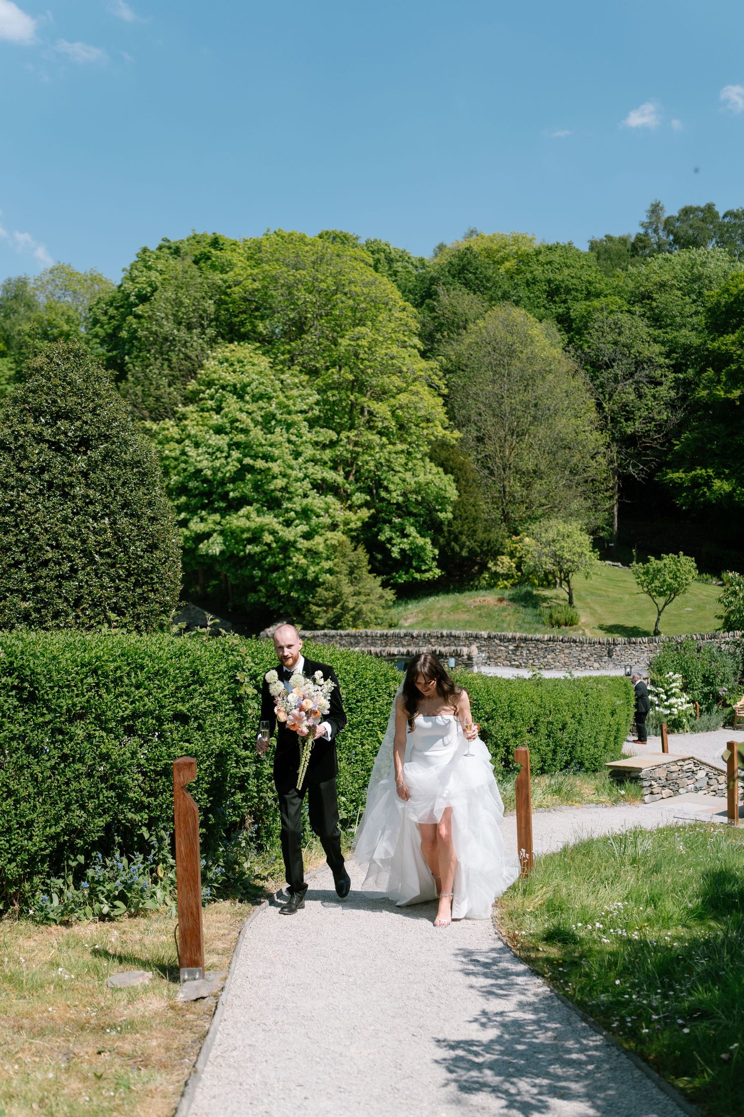 Bridal party walking down a winding garden path surrounded by green foliage.