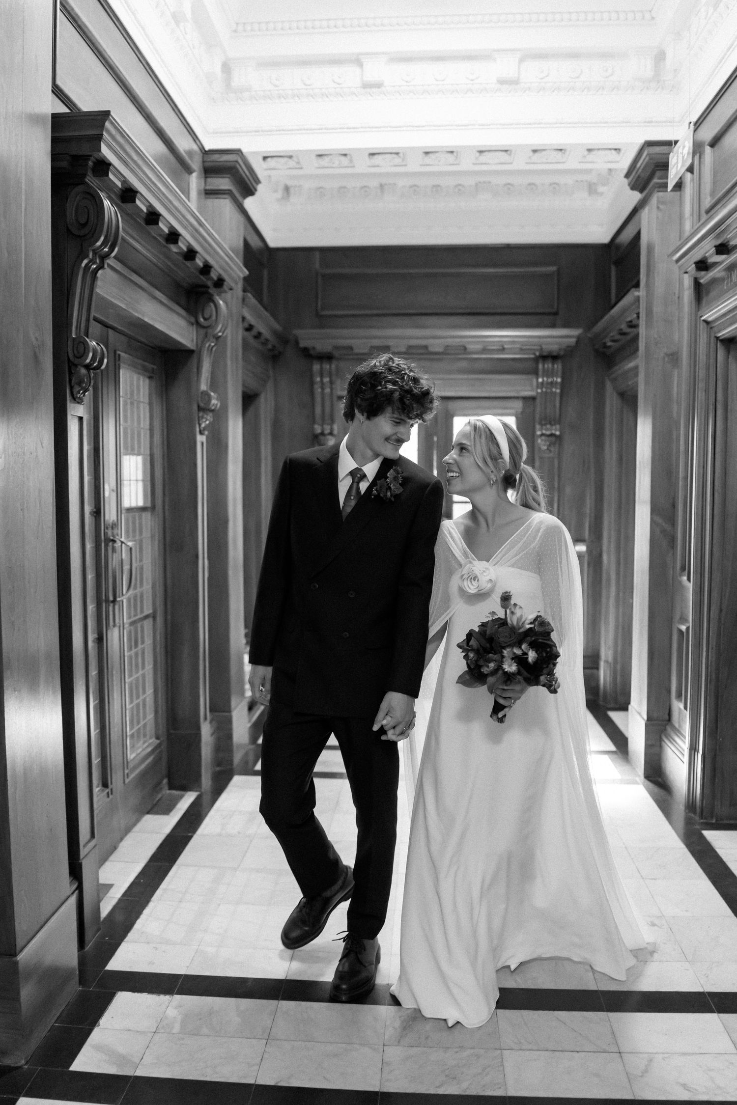 Black and white sequence of newlyweds walking together through a grand corridor.