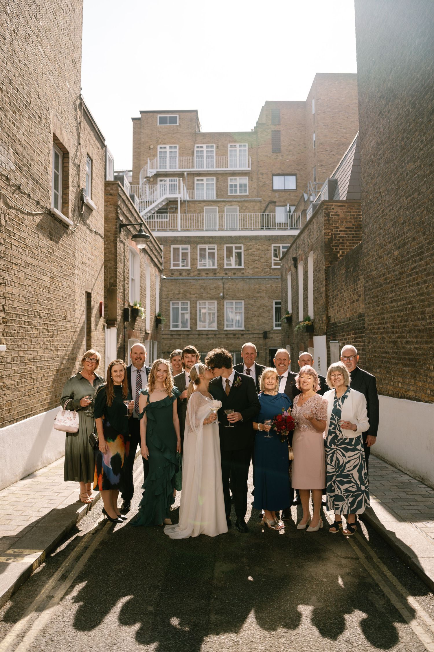 Wedding party group photo against brick wall backdrop in natural light.