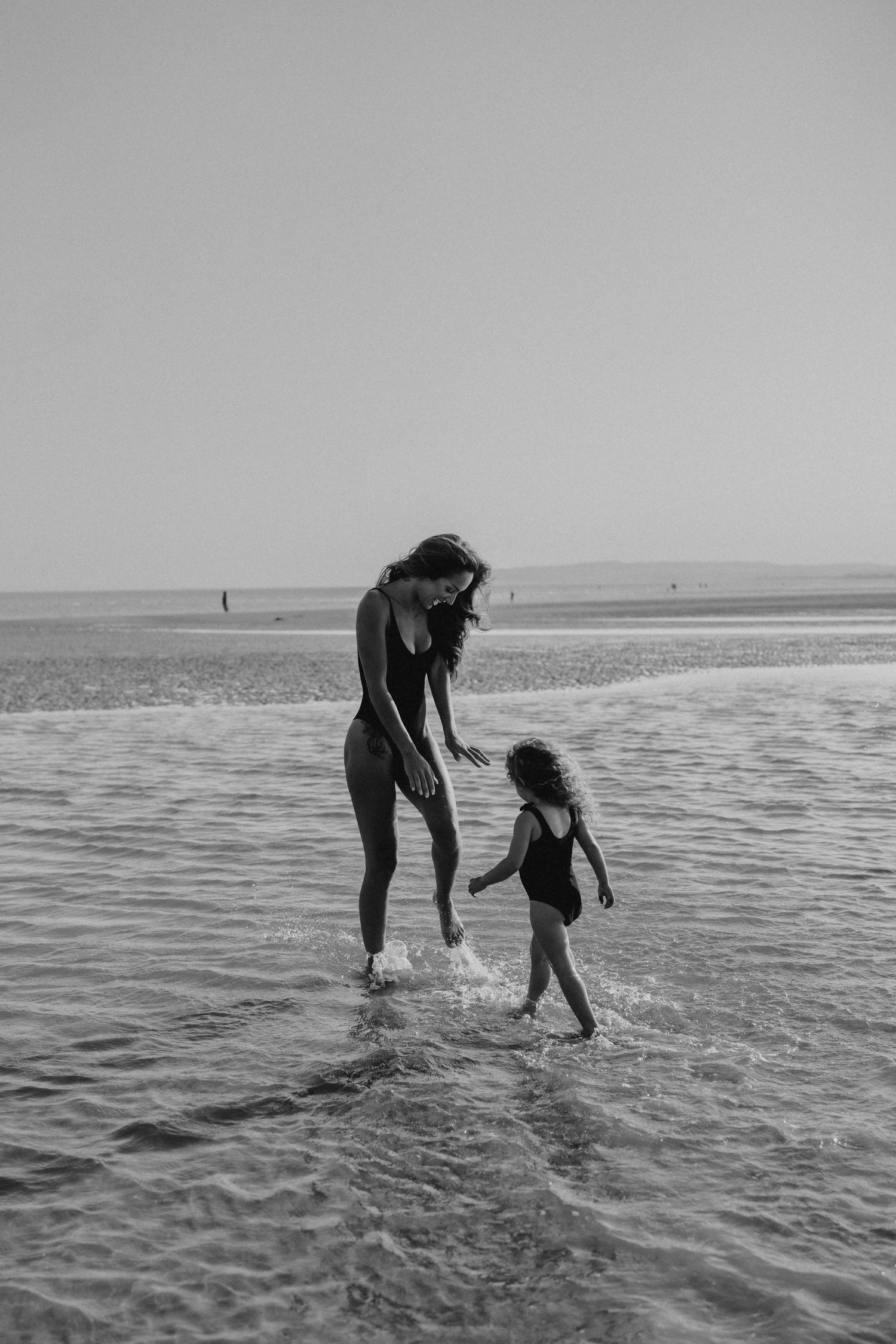 Black and white photo of two people jumping and splashing in shallow ocean waves.