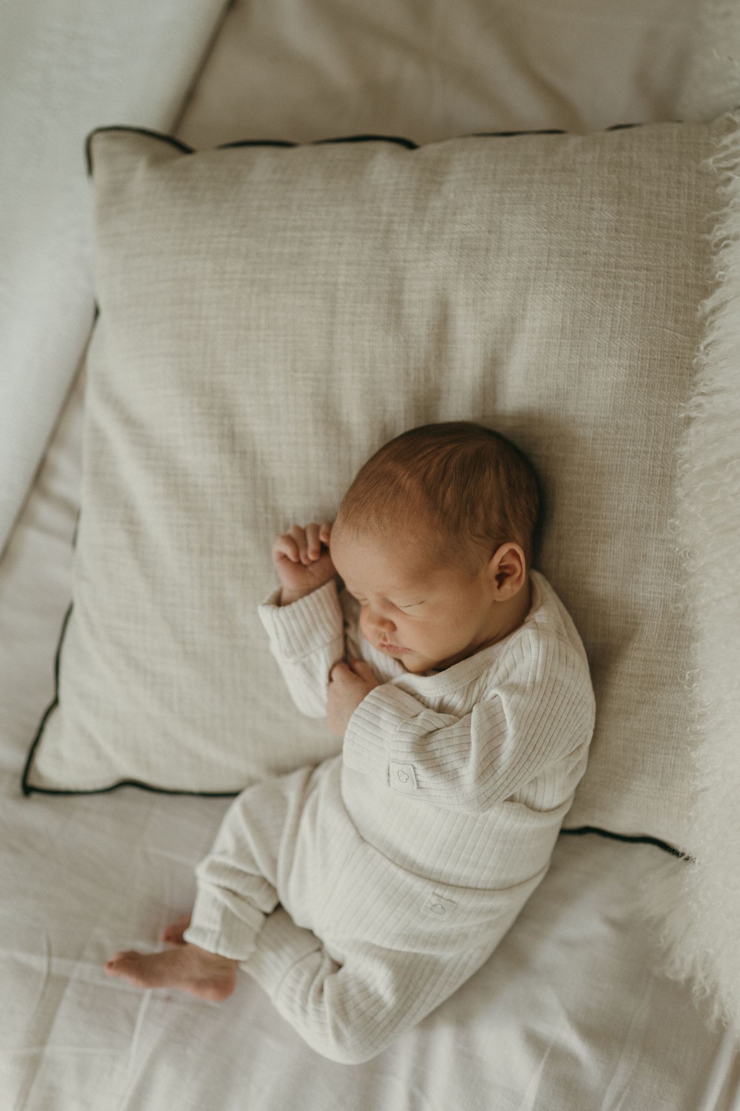 An infant in white clothing resting on a textured white bed.