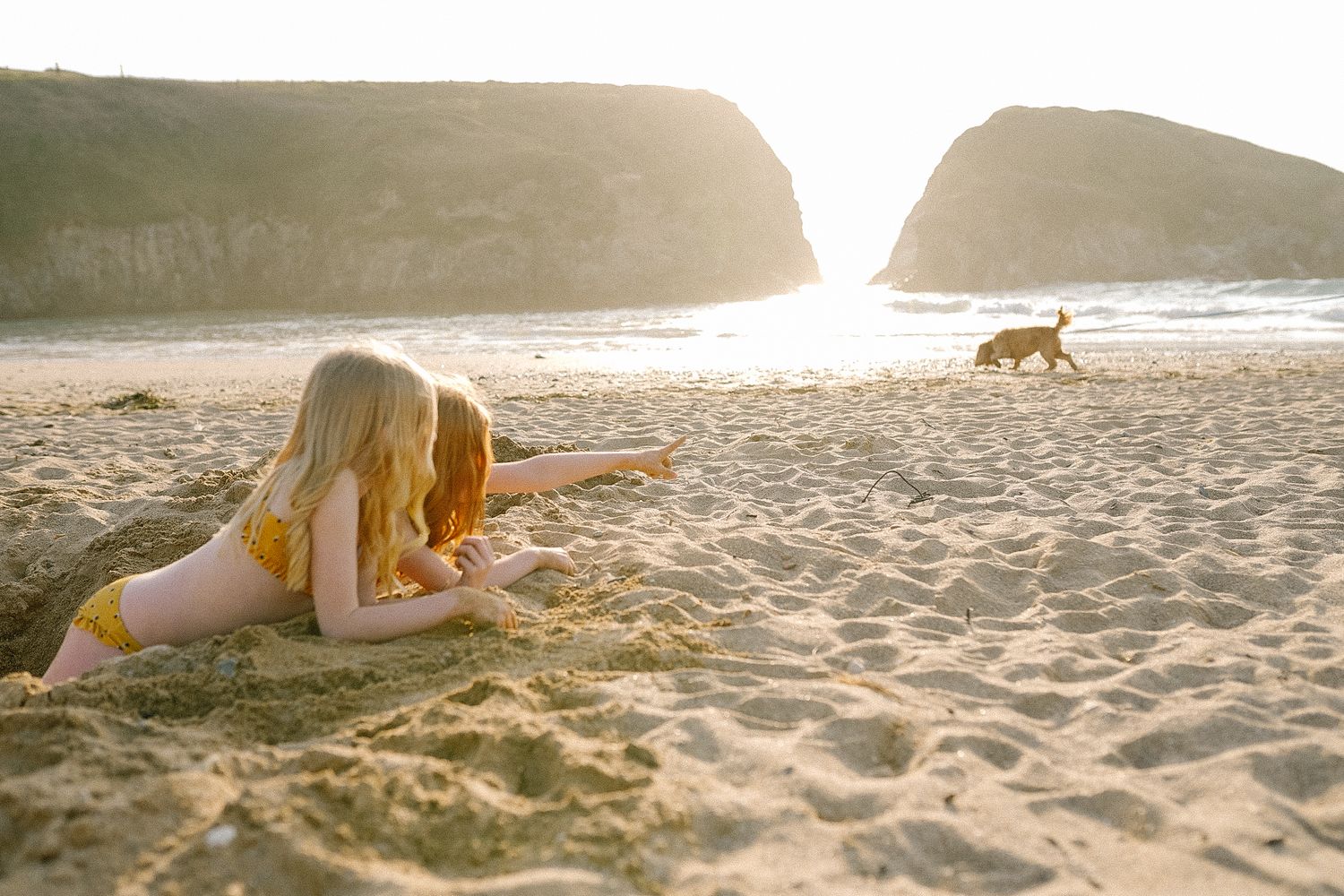 People lounging on golden sand beach with rocky cliffs and ocean waves.