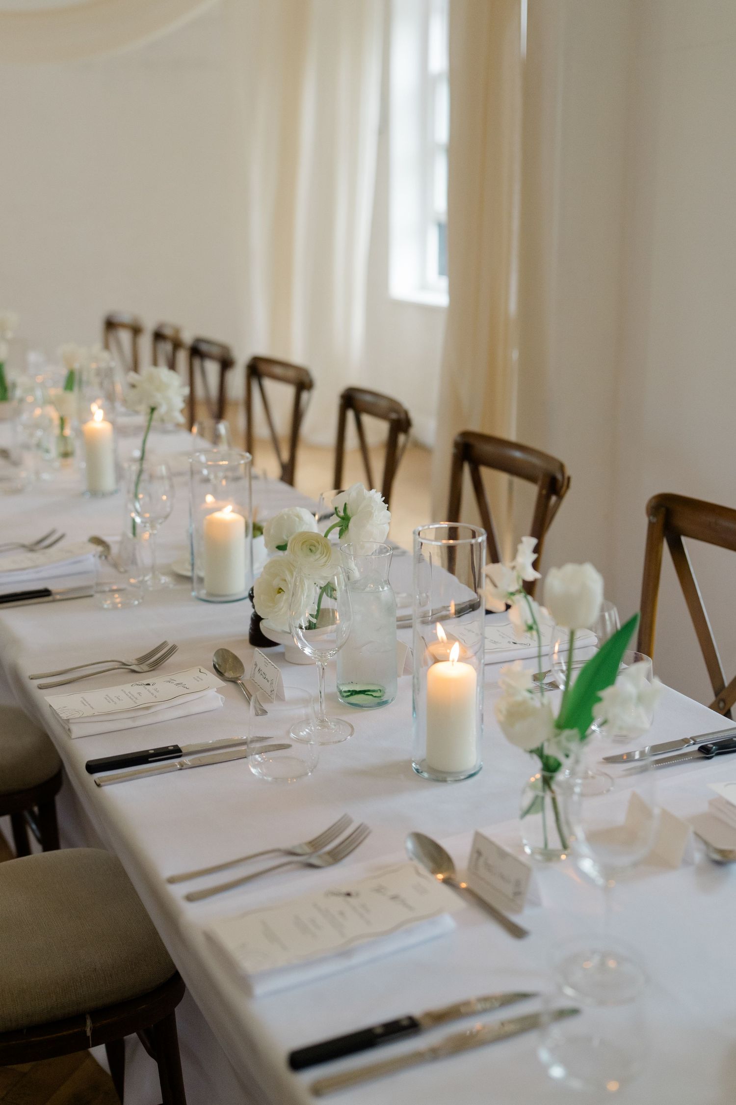 Elegant wedding reception table with white linens, candles, white floral arrangements and place settings.