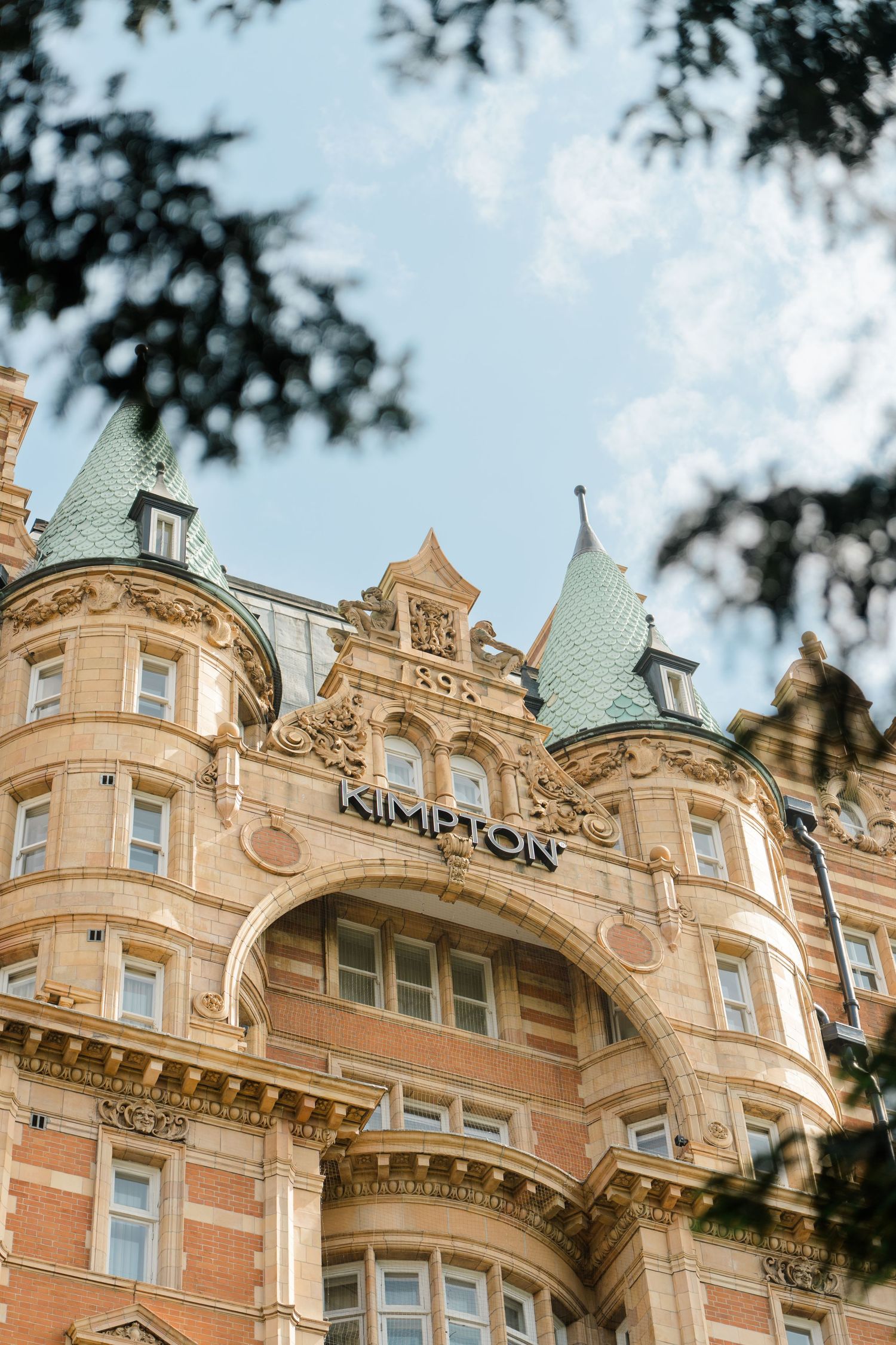 Kimpton hotel exterior featuring ornate Victorian architecture with green copper turrets against a blue sky.