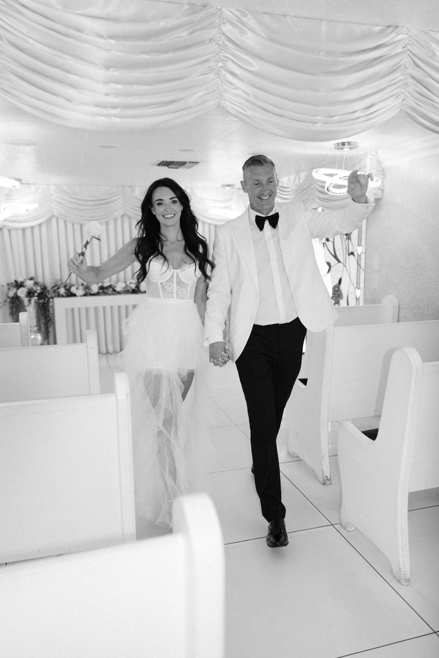Wedding couple walks through elegant white draped room.