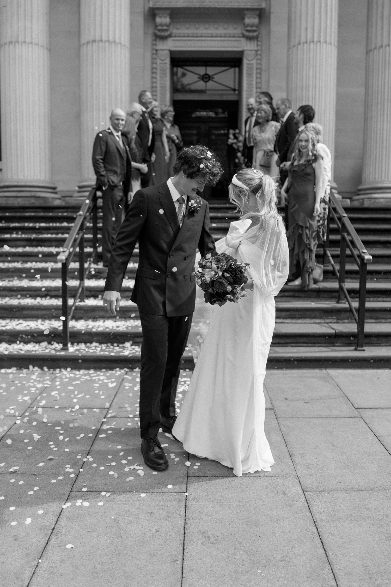 Wedding couple walks together through scattered confetti on stone steps.