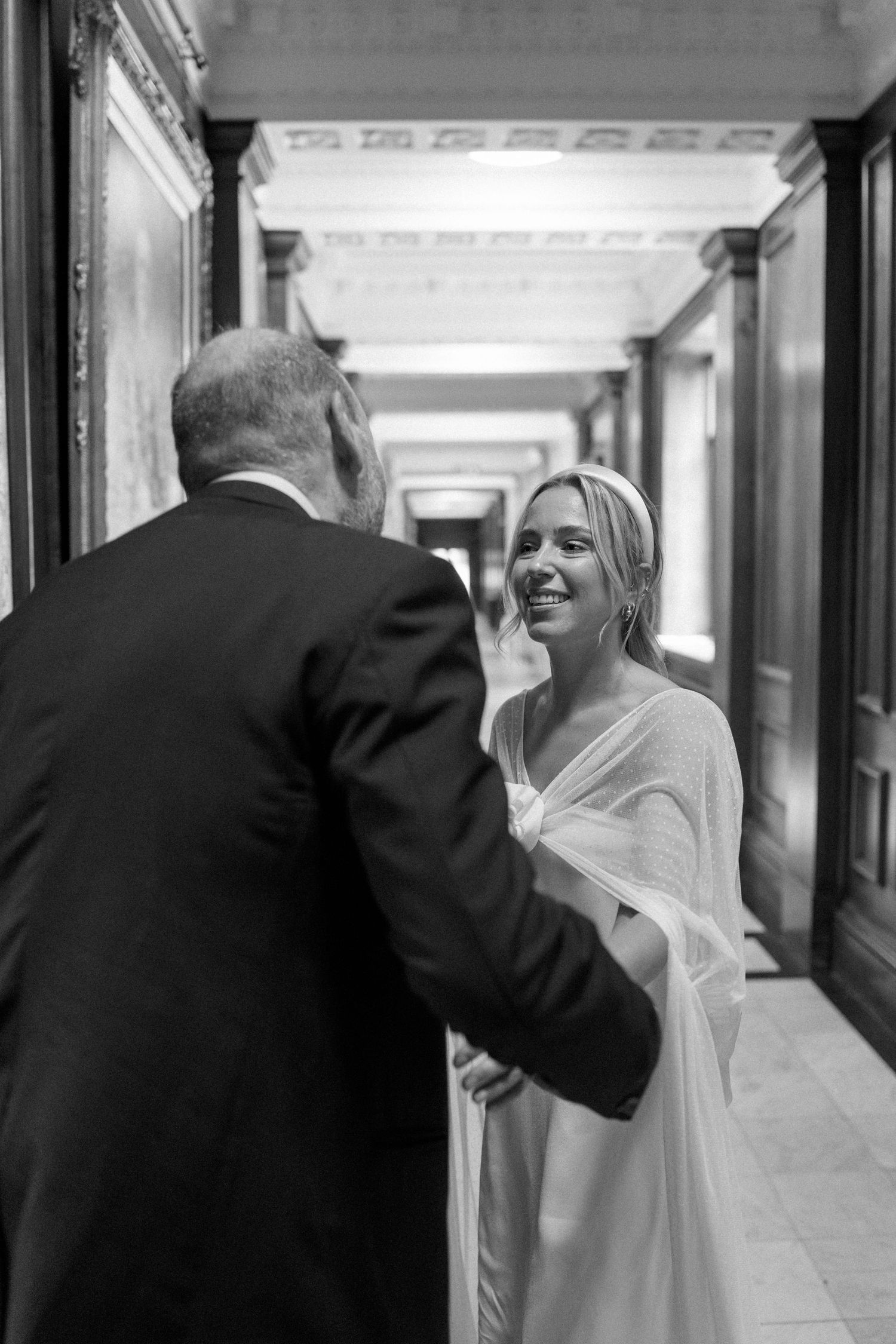Black and white candid moment in a hallway during a wedding celebration.
