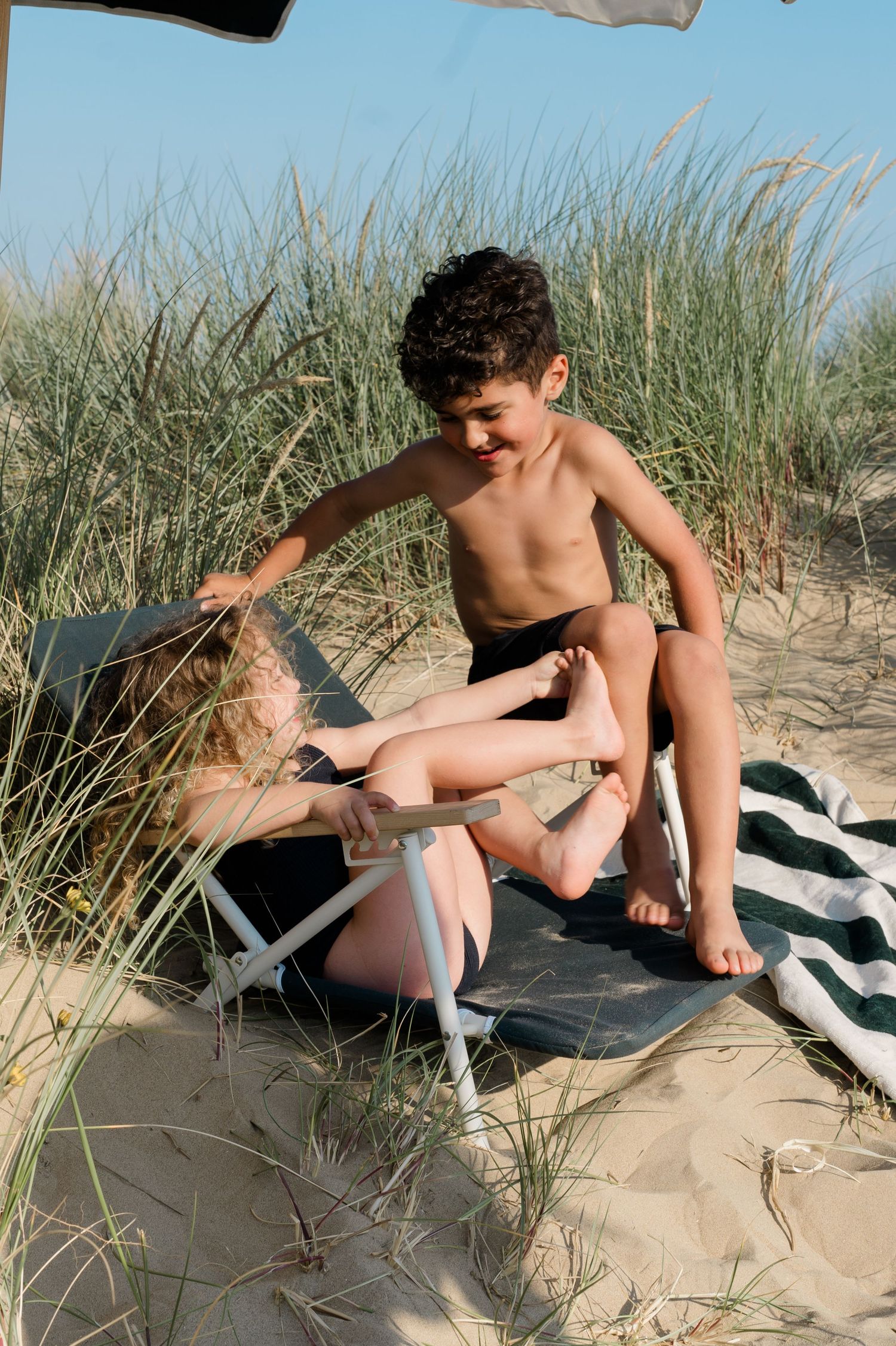 Relaxing under beach umbrella on striped towel among sand dunes and beach grass.