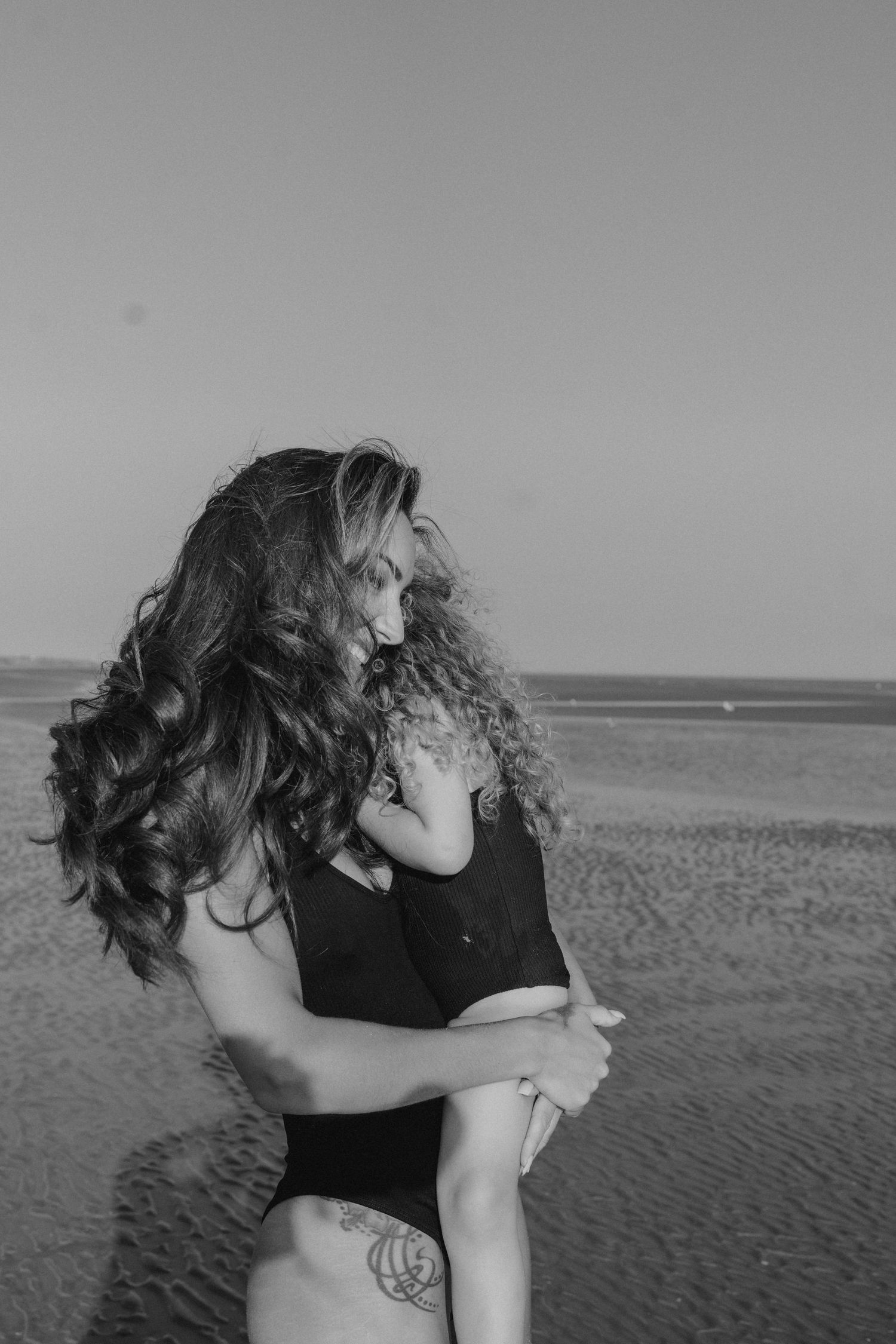 Black and white photo of people embracing on a beach at sunset.