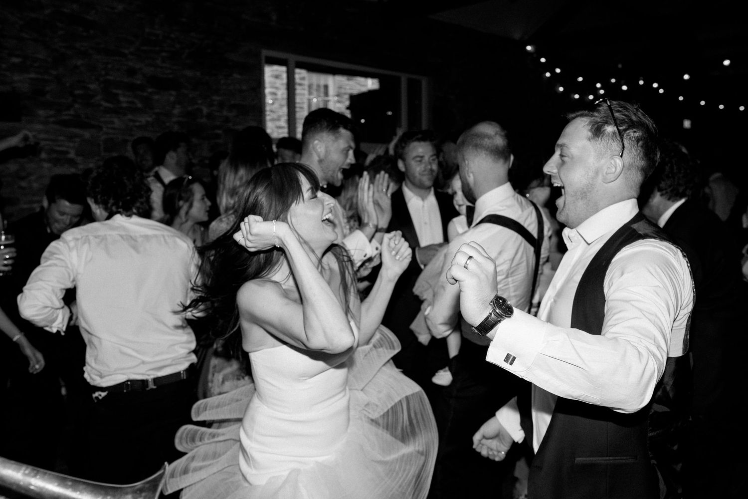 Wedding guests dance and celebrate on the reception dance floor in black and white.