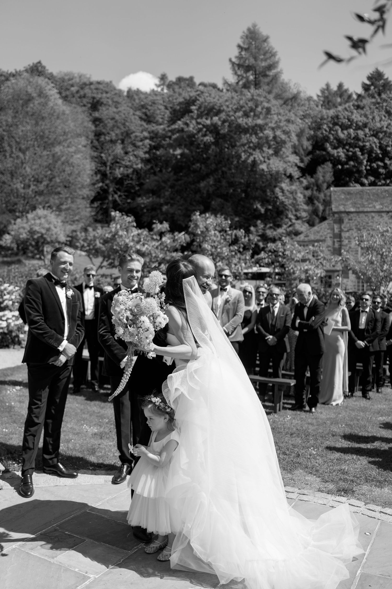 Wedding party walks down a stone path in a garden setting during an outdoor ceremony.