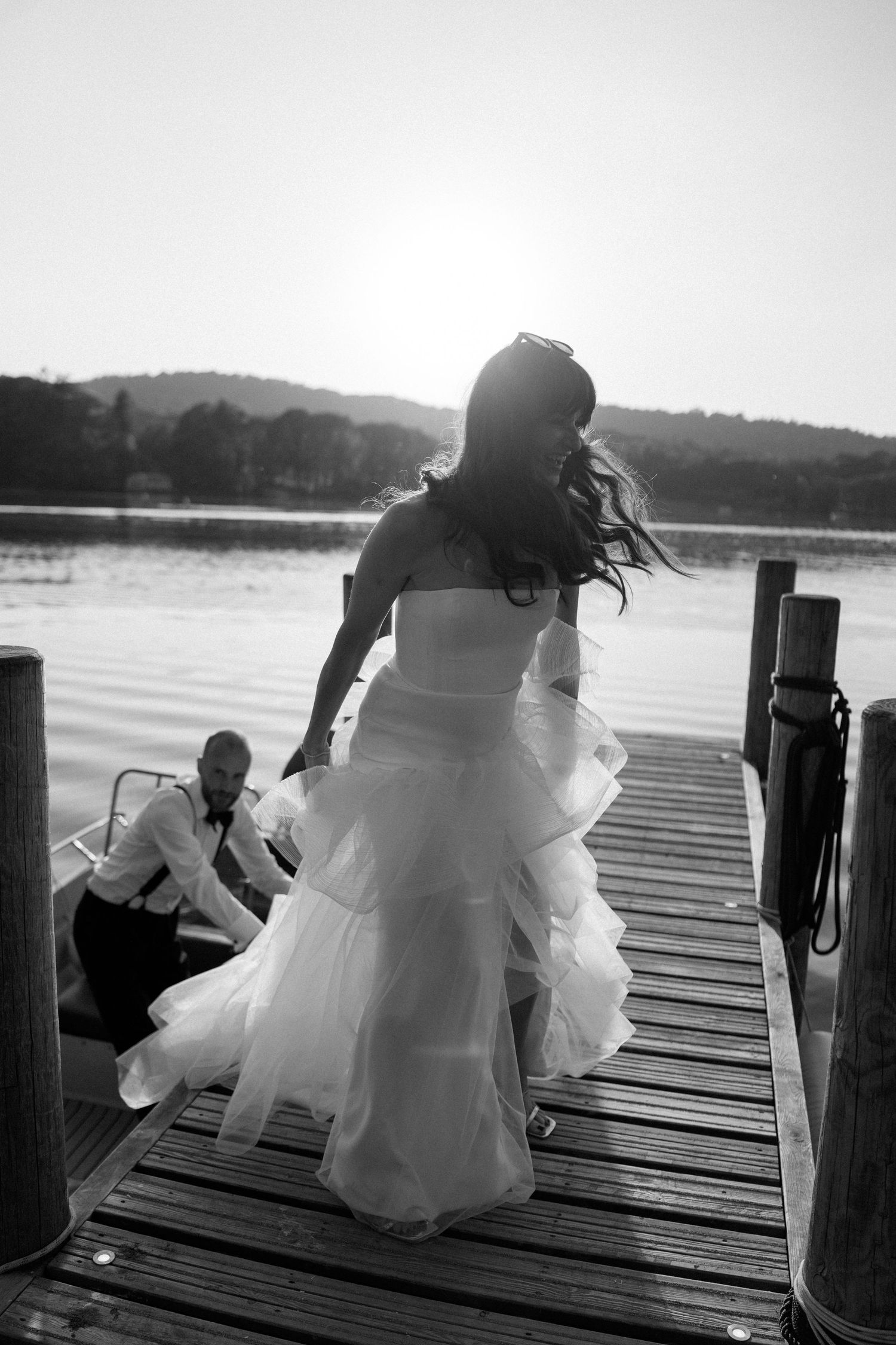 Black and white photo of a couple in formal wear posing dramatically on a wooden pier.
