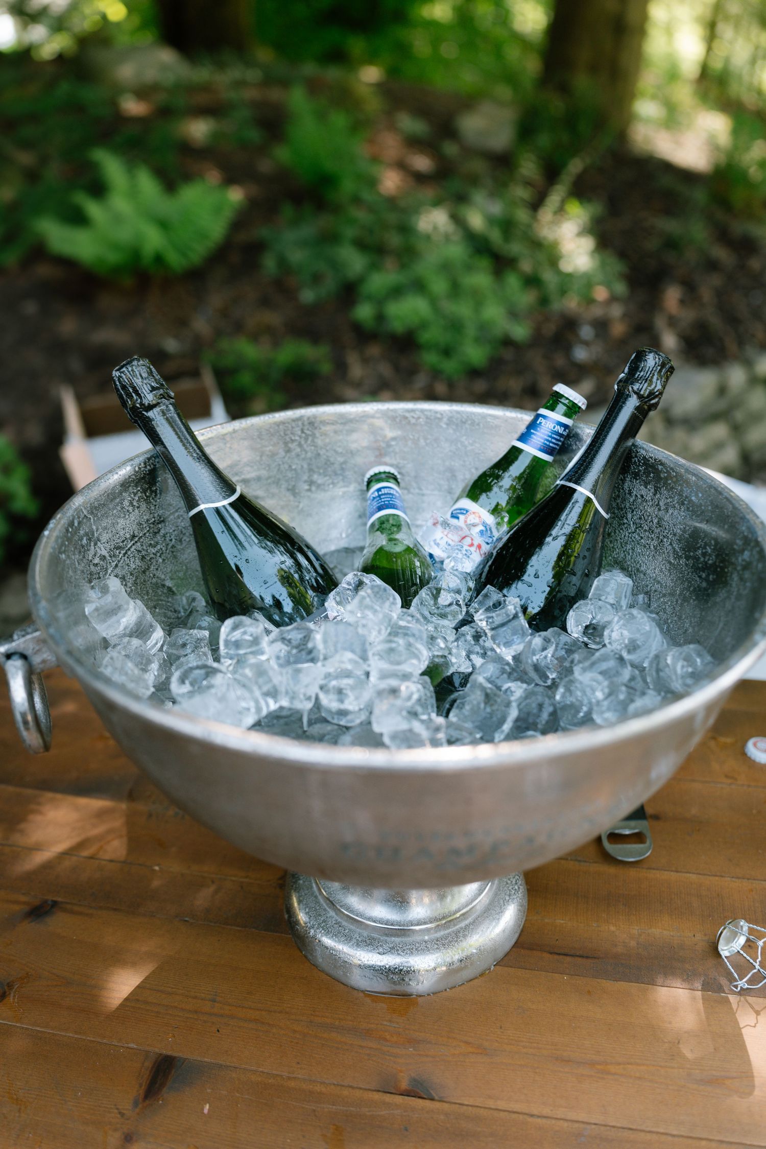 Silver champagne bowl filled with ice and bottles at an outdoor event.