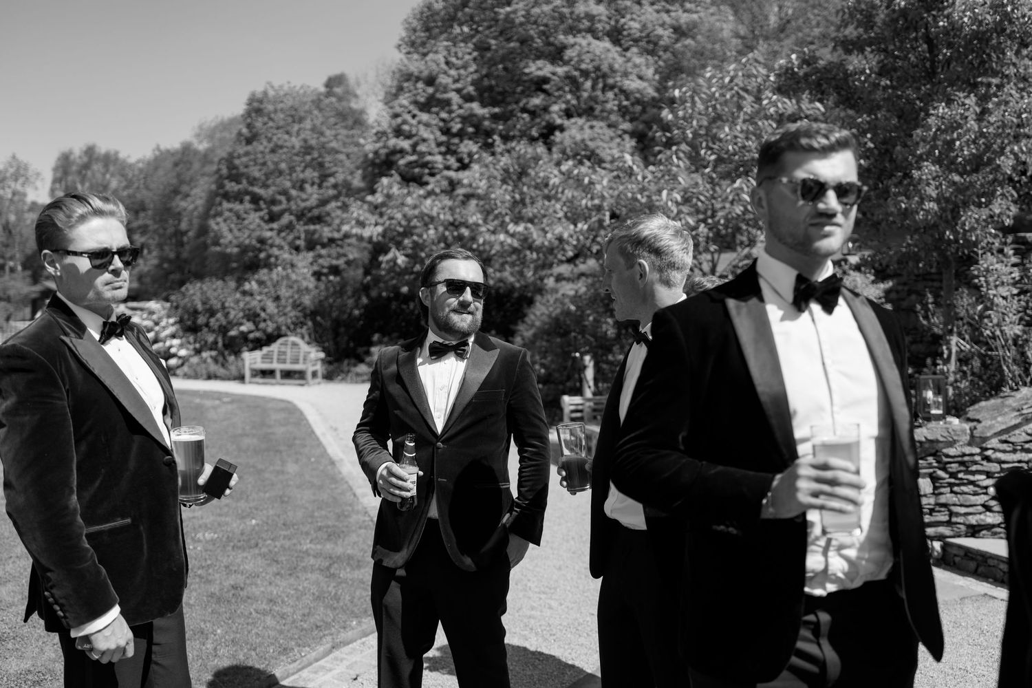 Groomsmen in tuxedos gathered outside on a sunny day.