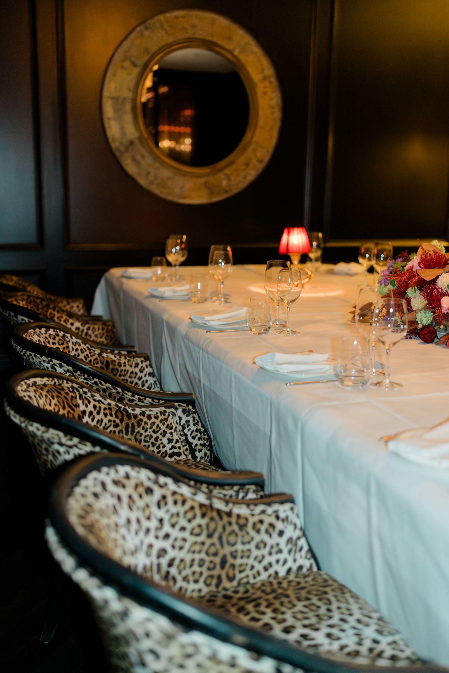 Elegant wedding reception table with white linen, crystal glasses, leopard print chairs, and floral centerpiece.