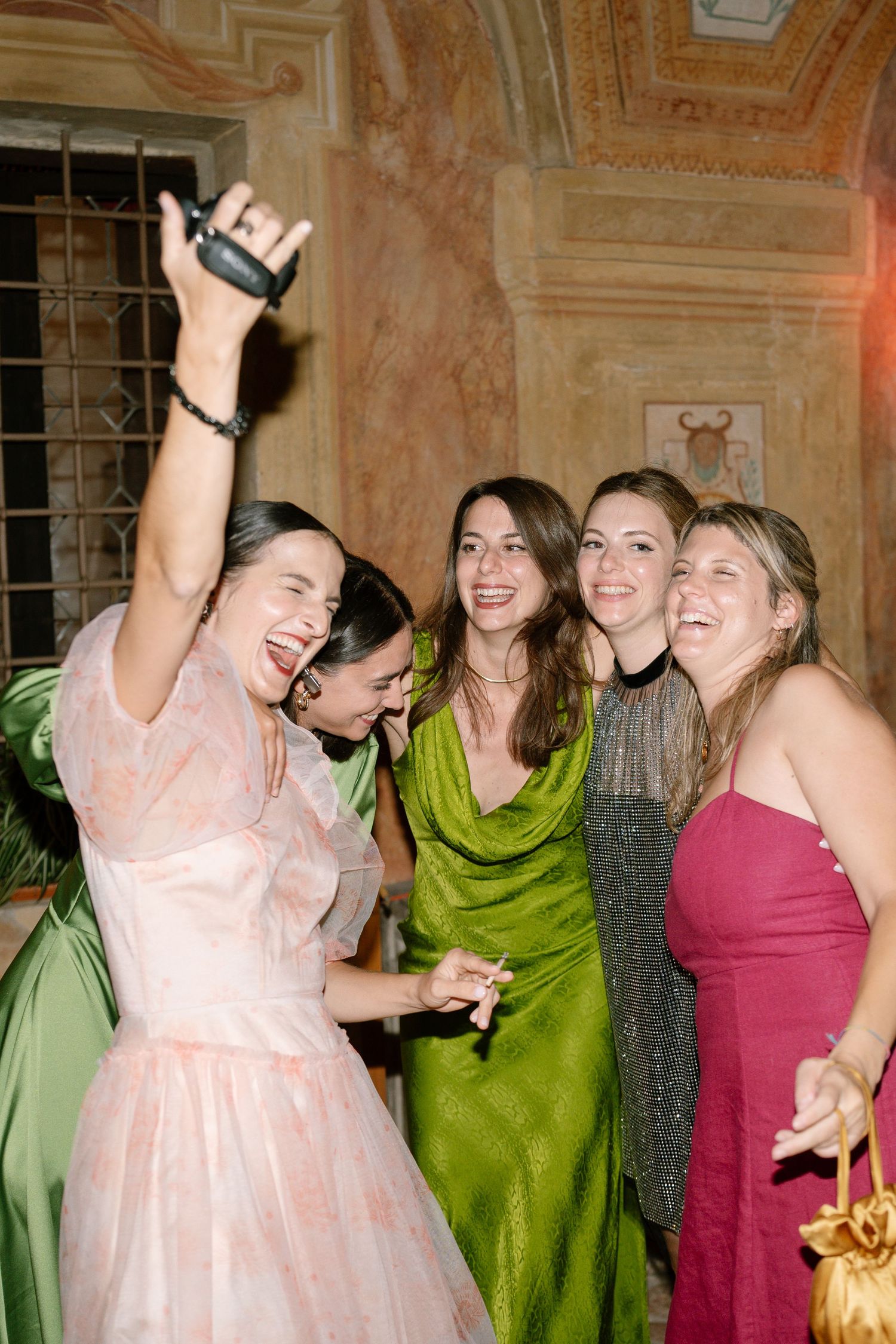 Group of friends celebrating in colorful dresses at an elegant party venue with decorative walls.