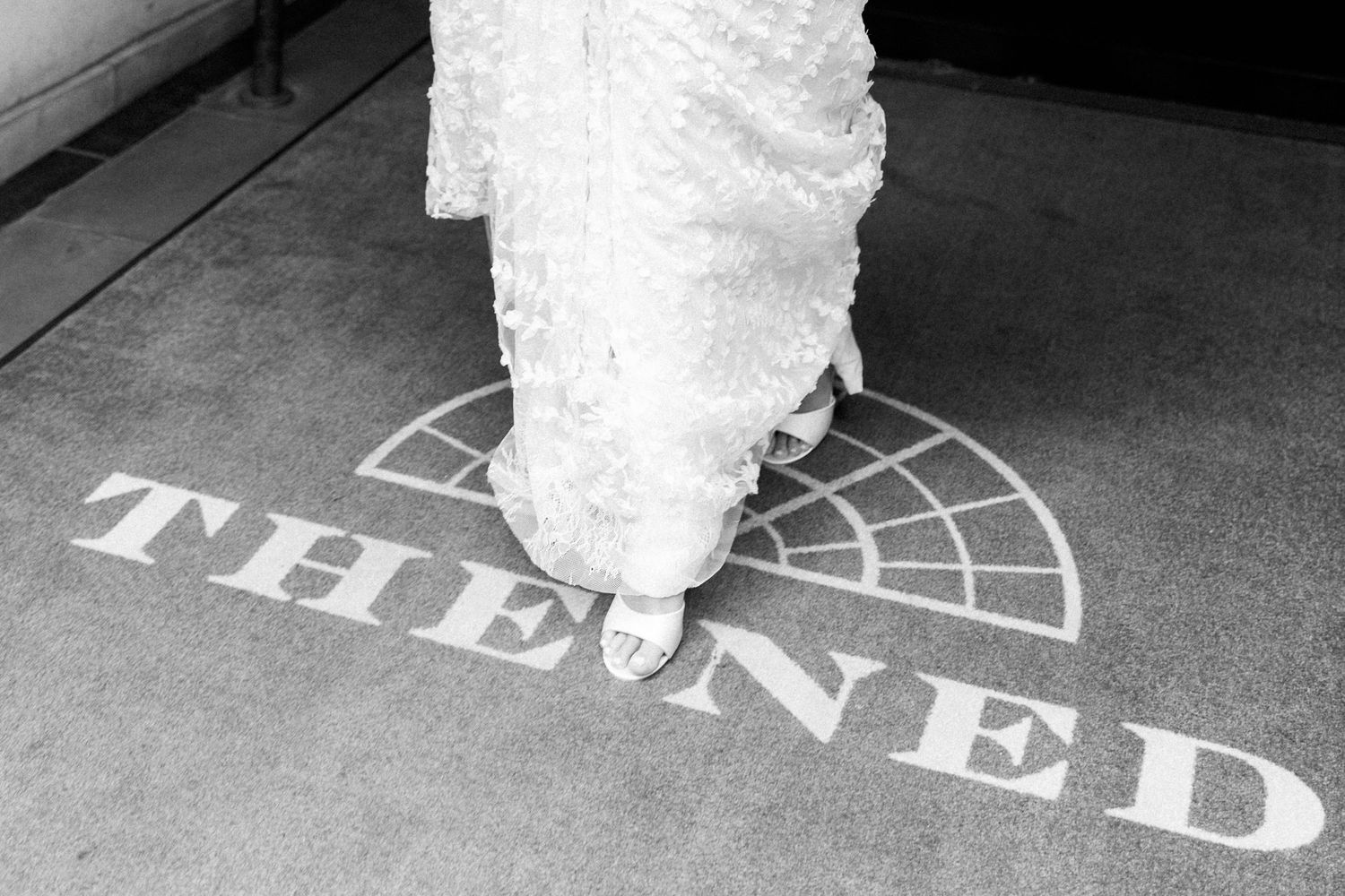 Close-up of bride's white lace dress hem against patterned floor.