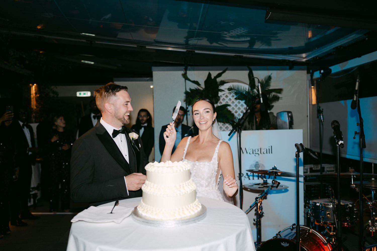 Couple sharing laughs while cutting their traditional white wedding cake.