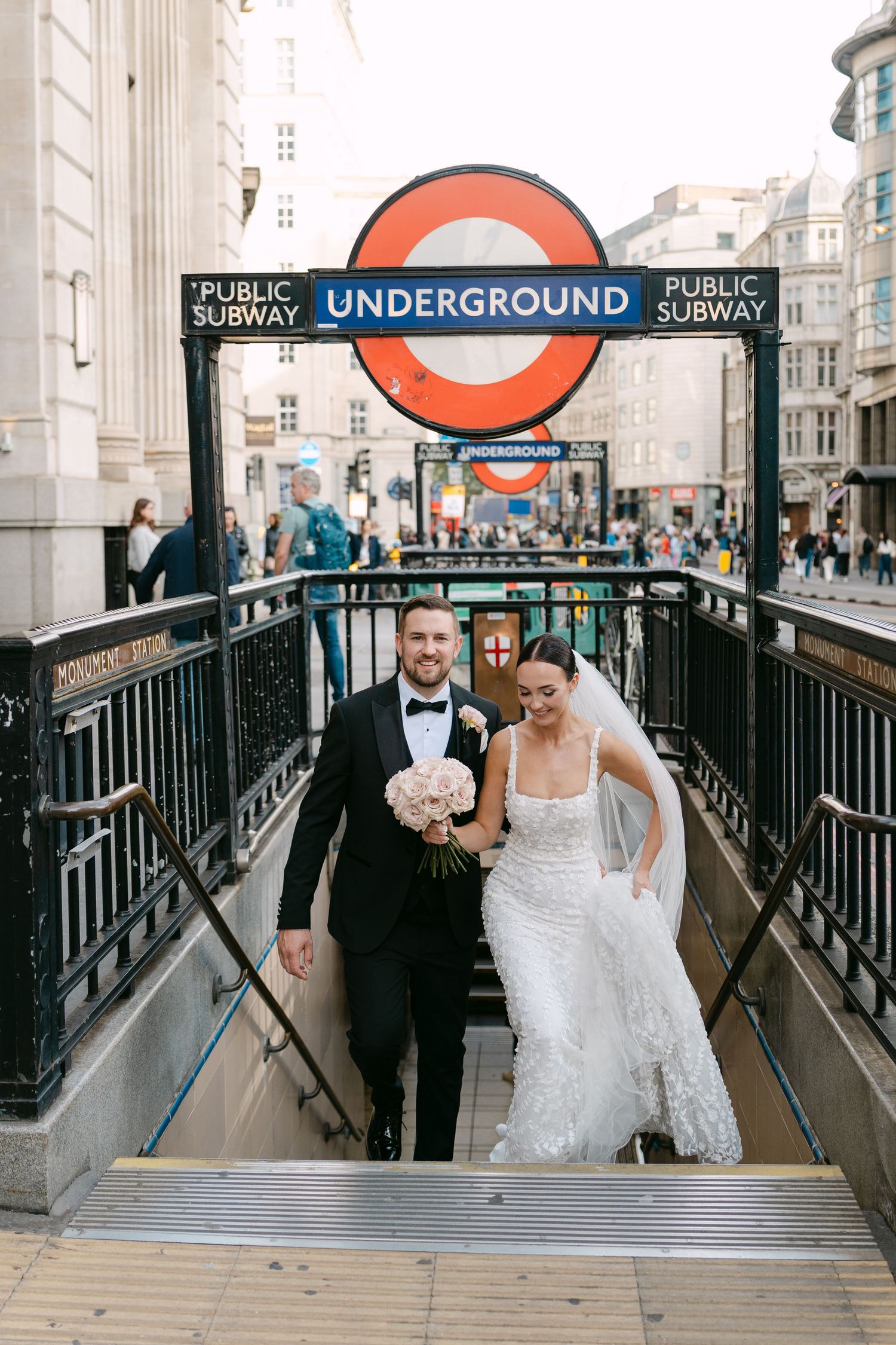 A wedding couple descends the stairs at a London Underground station entrance.
