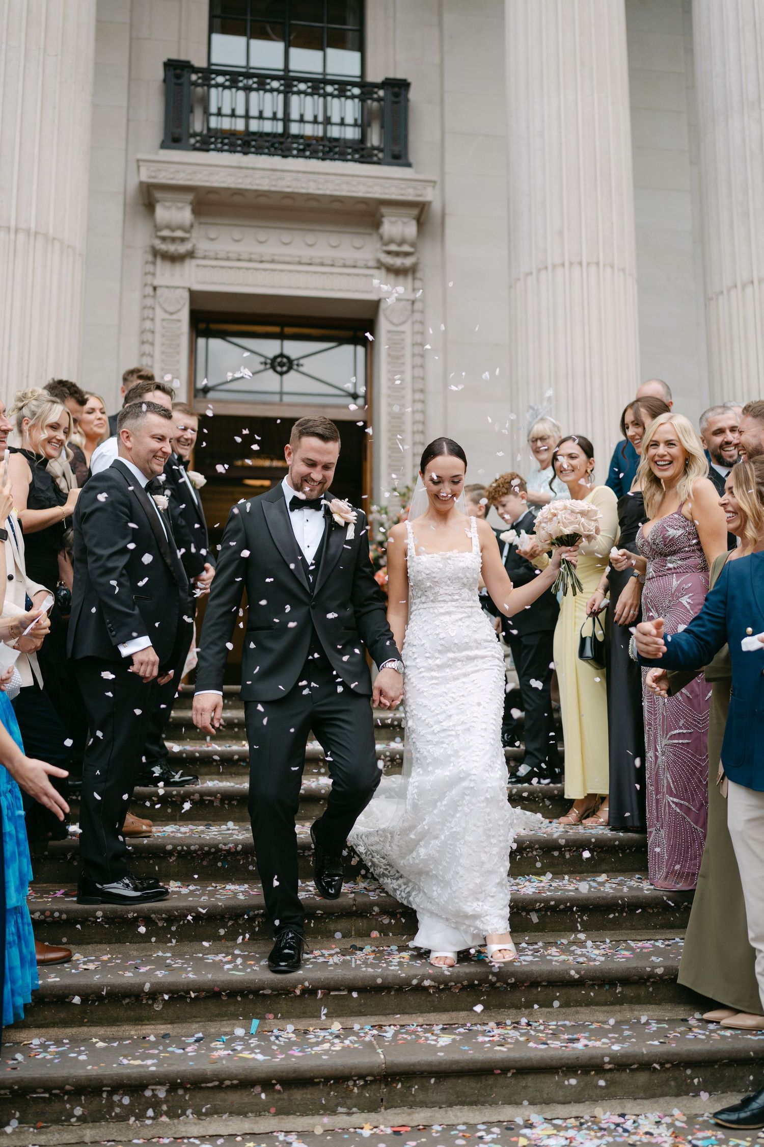 Wedding celebration with confetti shower outside historic building with columns.