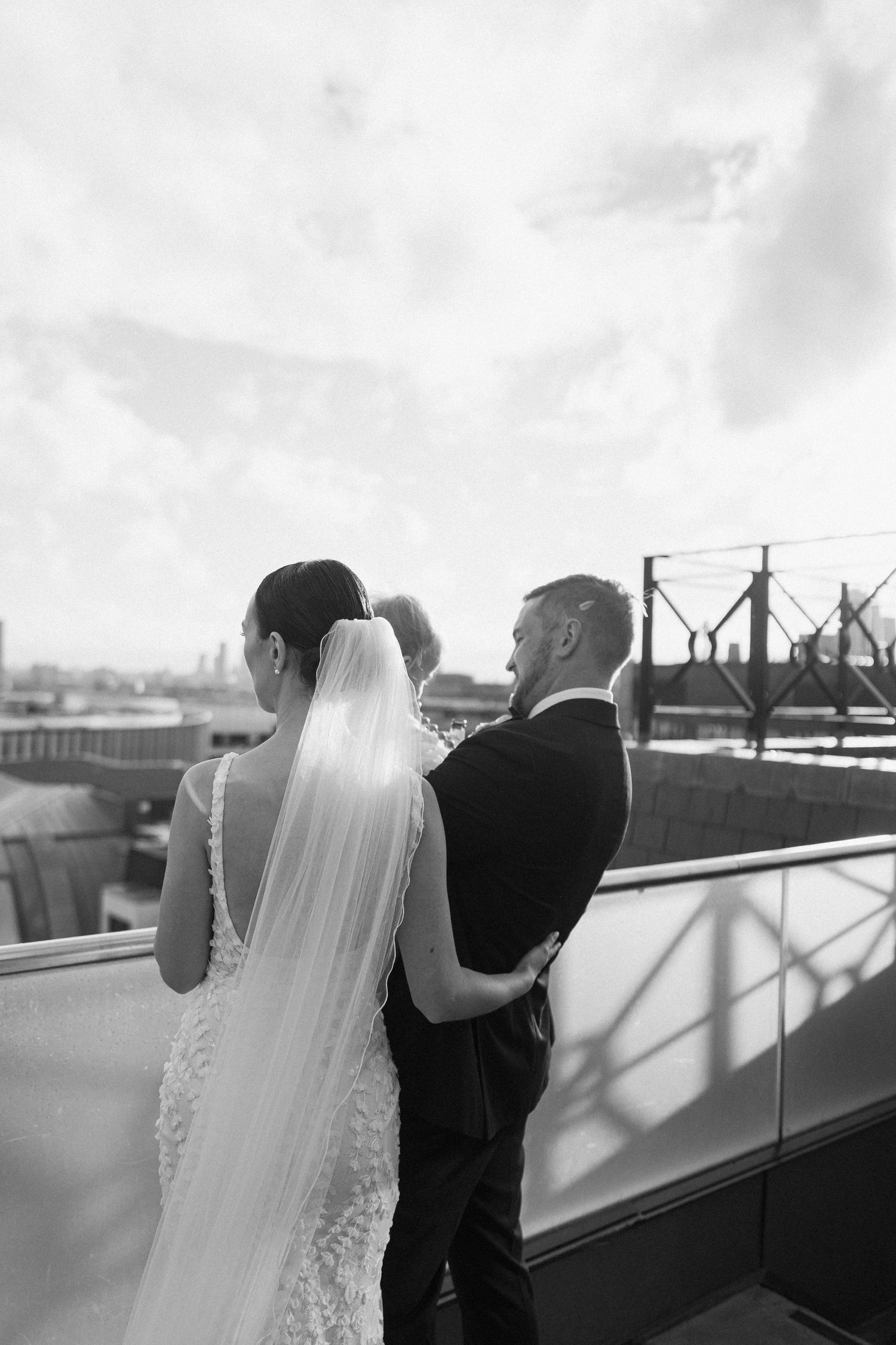 Black and white photo of a couple in wedding attire sharing an intimate moment on a city rooftop.