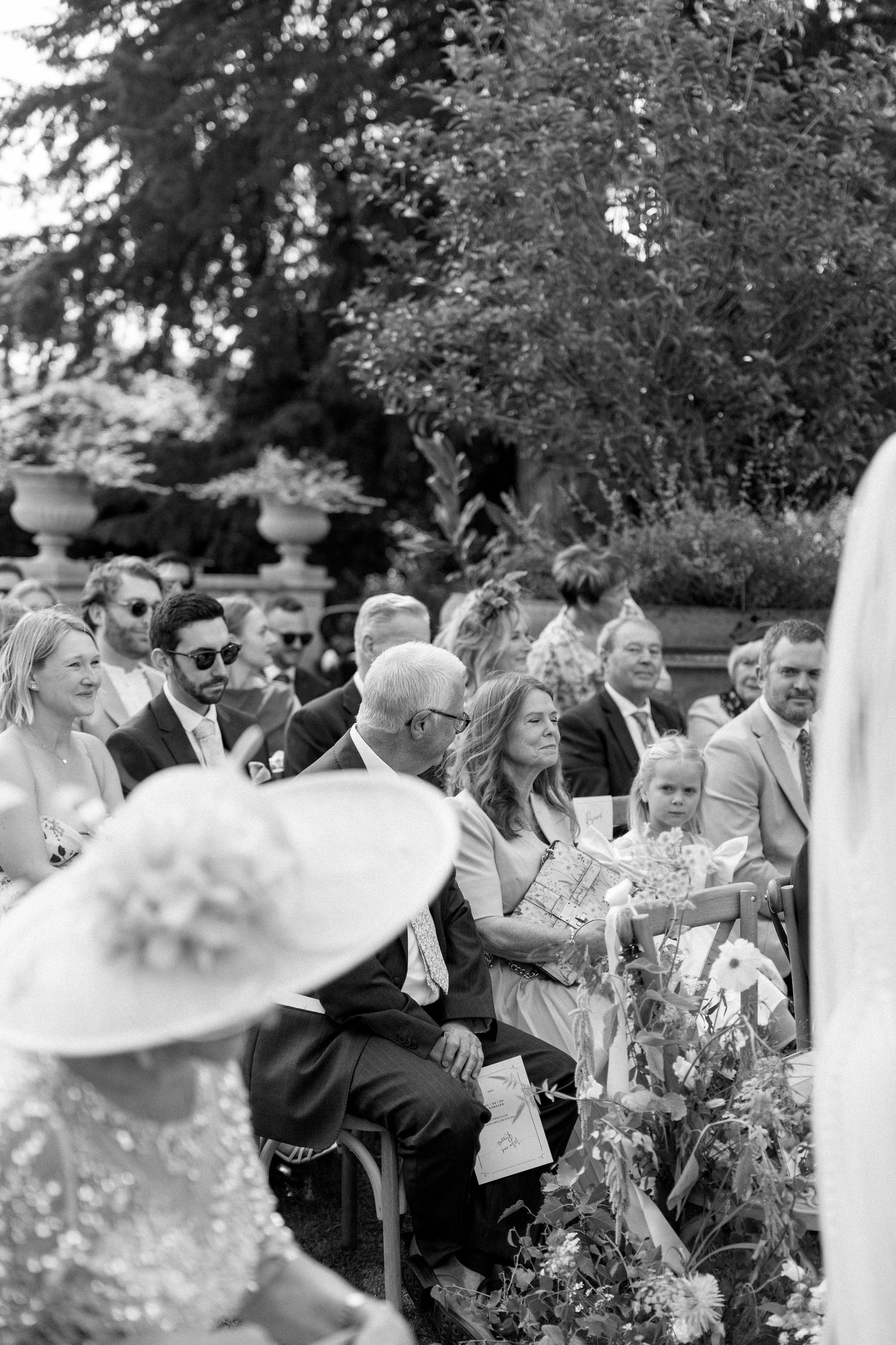 Black and white photo of wedding guests seated outdoors during a garden ceremony.