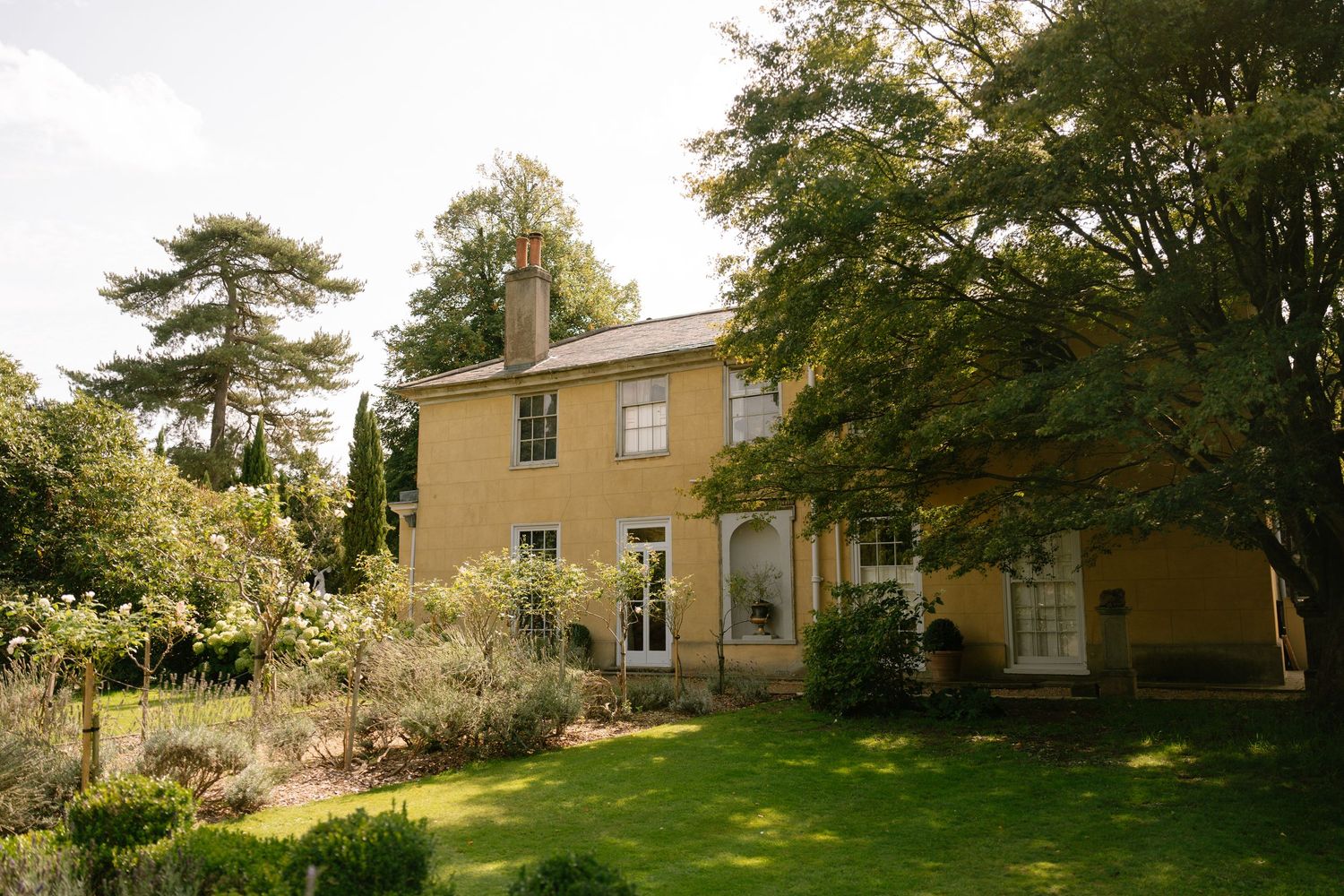 Yellow Georgian style country house with large windows and mature trees in the garden.
