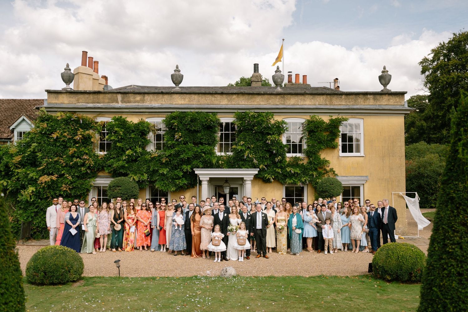 Panoramic view of wedding guests lined up outside a grand country house.