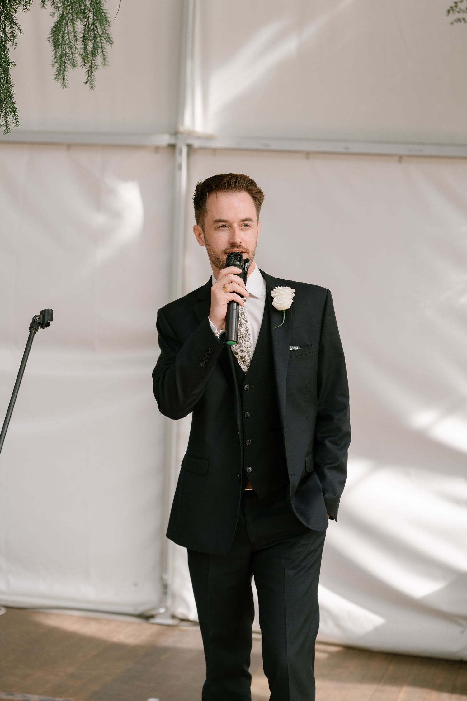 A formal speaker addresses guests during a wedding reception in a tent venue.