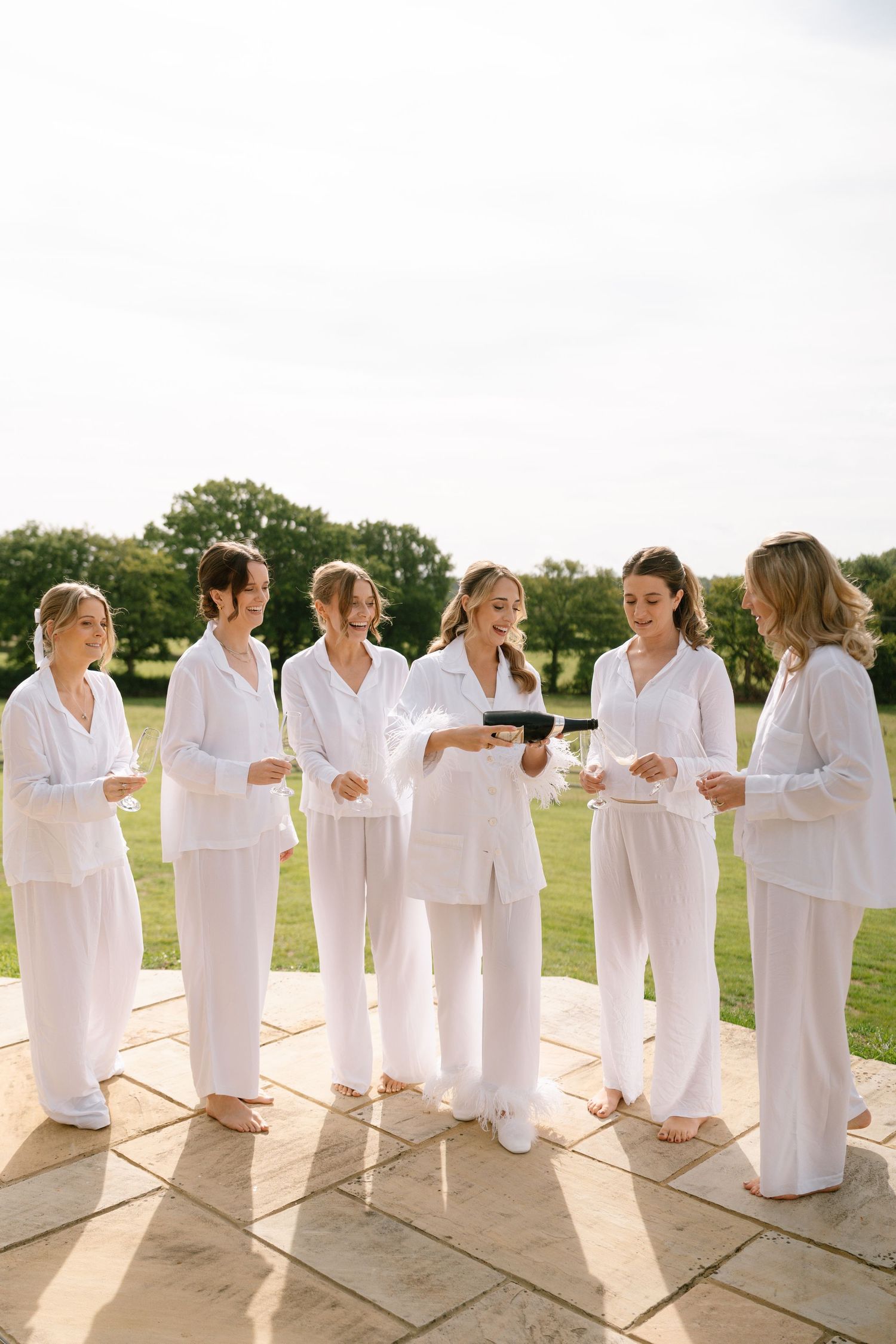 A group wearing coordinated white ensembles gathers on a stone patio for celebration photos.
