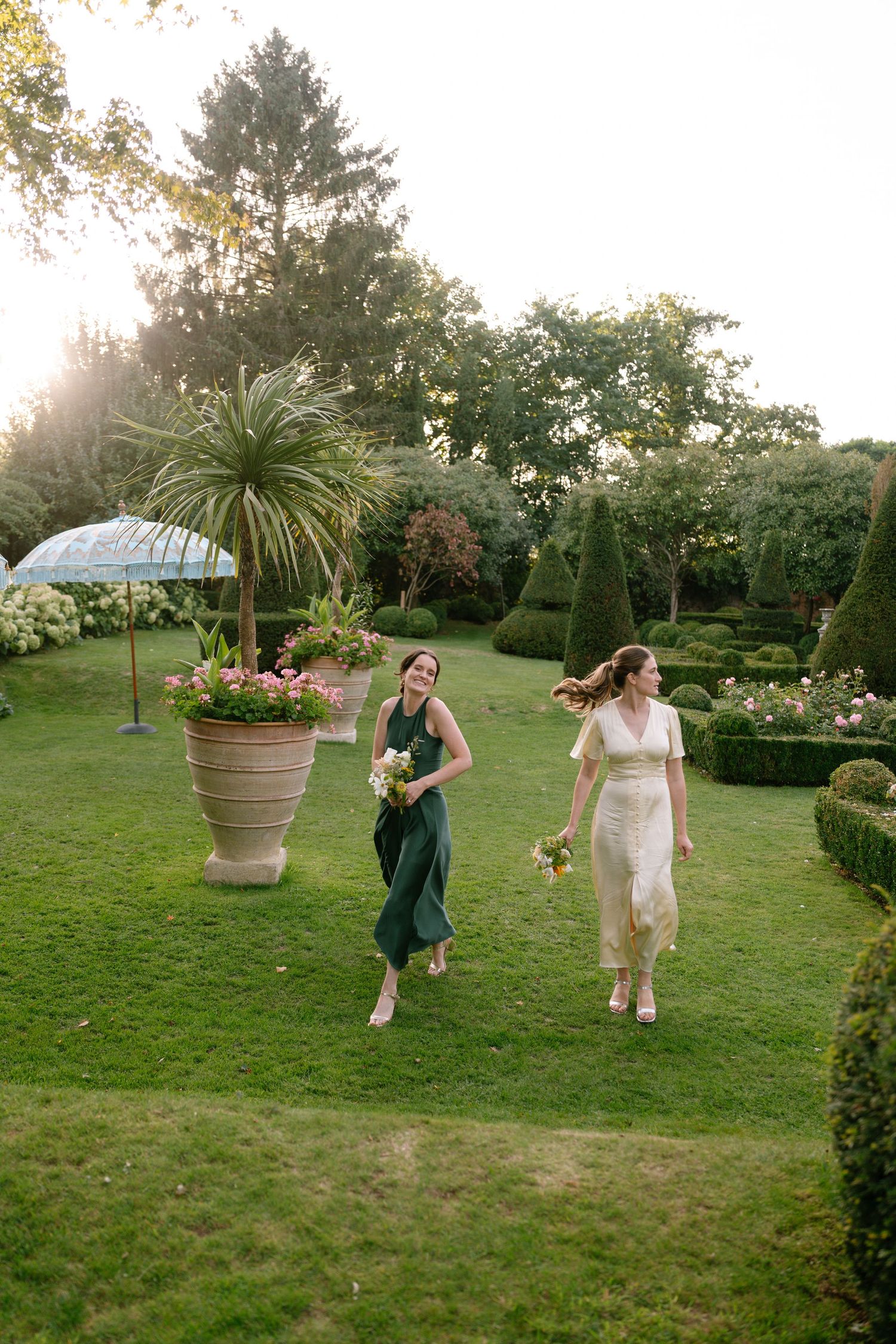 A group dances and celebrates on a manicured lawn with potted plants and garden decor.