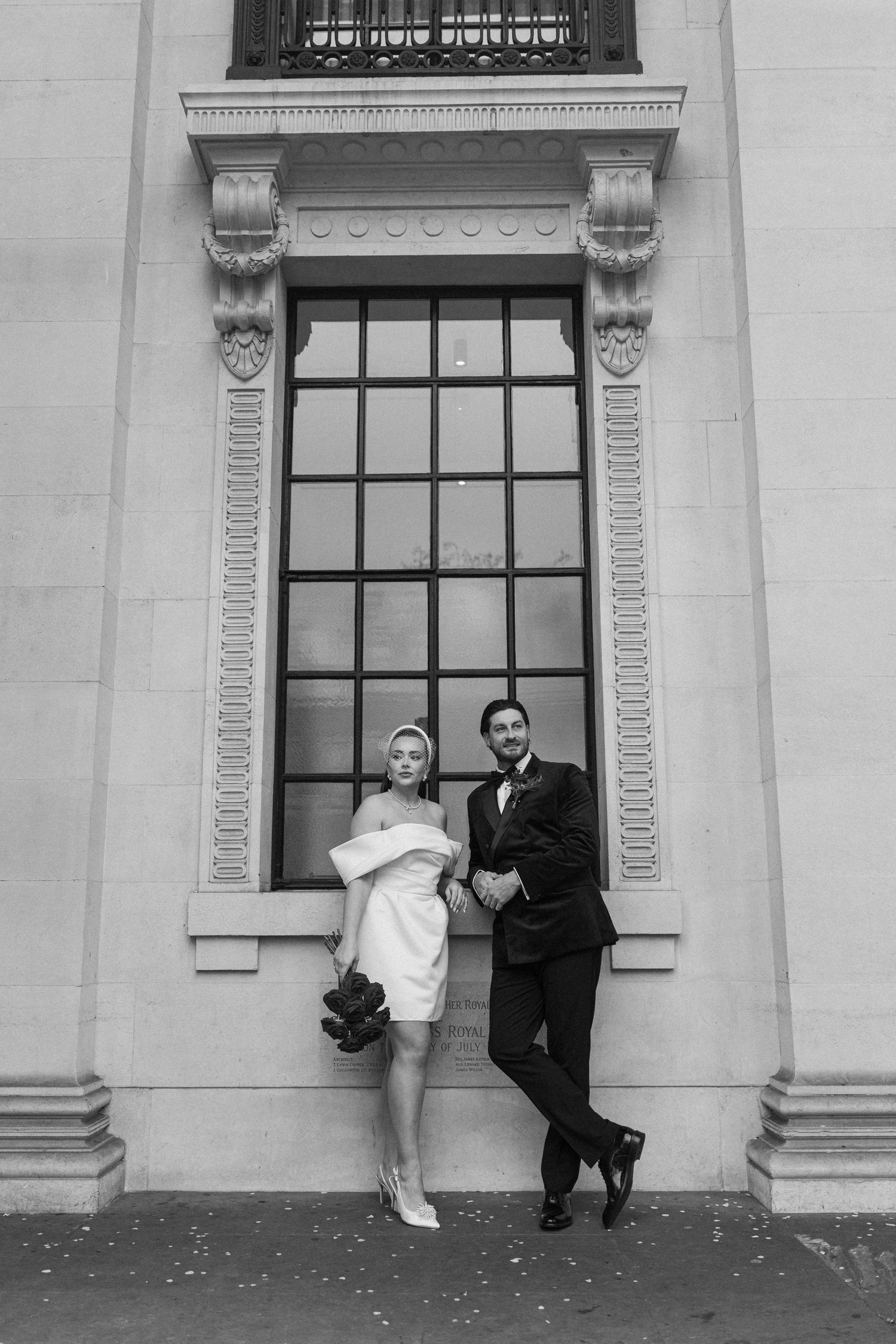 Playful black and white wedding portraits showing couple posing against a classical building window.