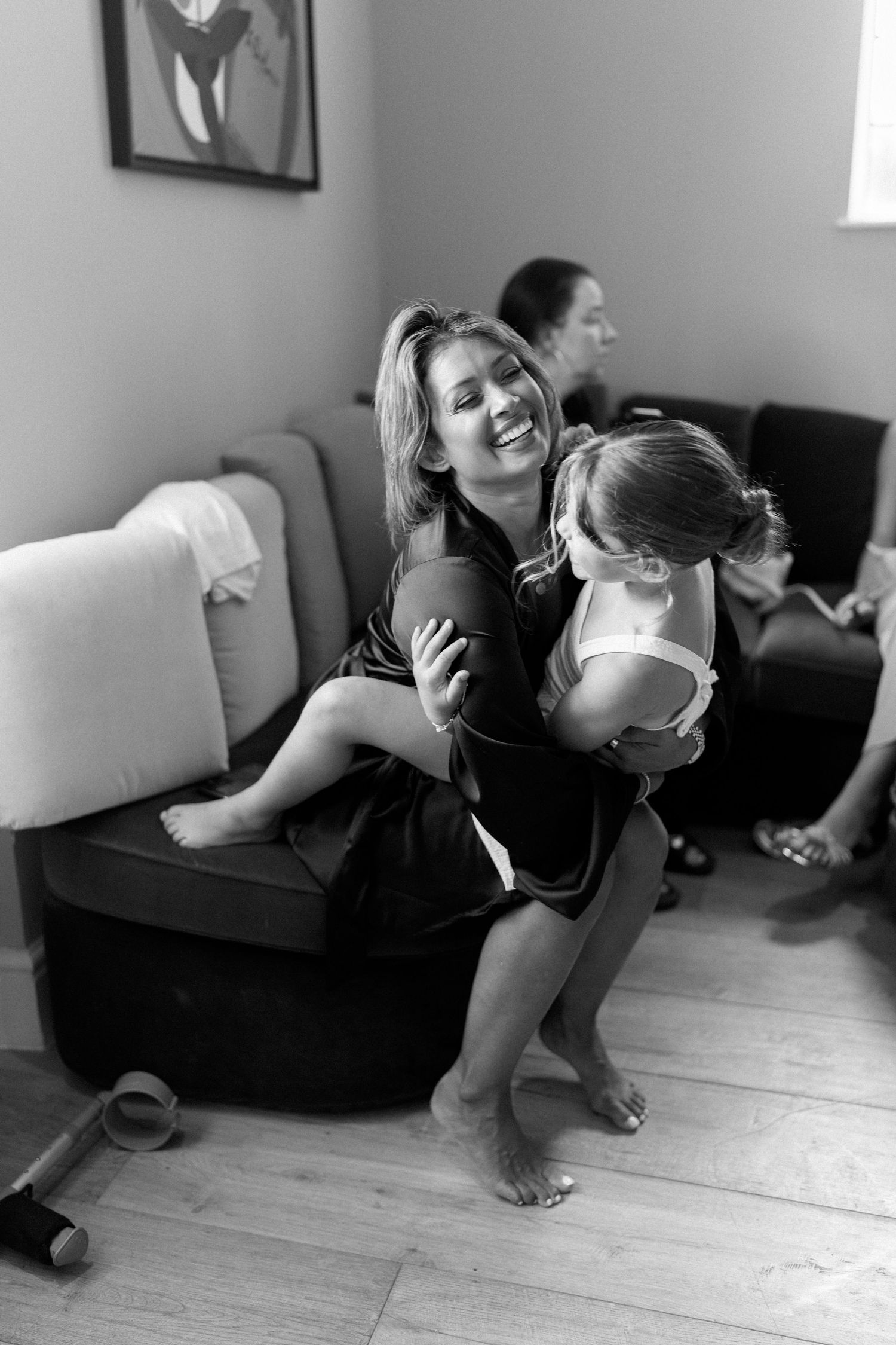 Black and white photo of smiling woman in robe holding laughing child during wedding preparations.