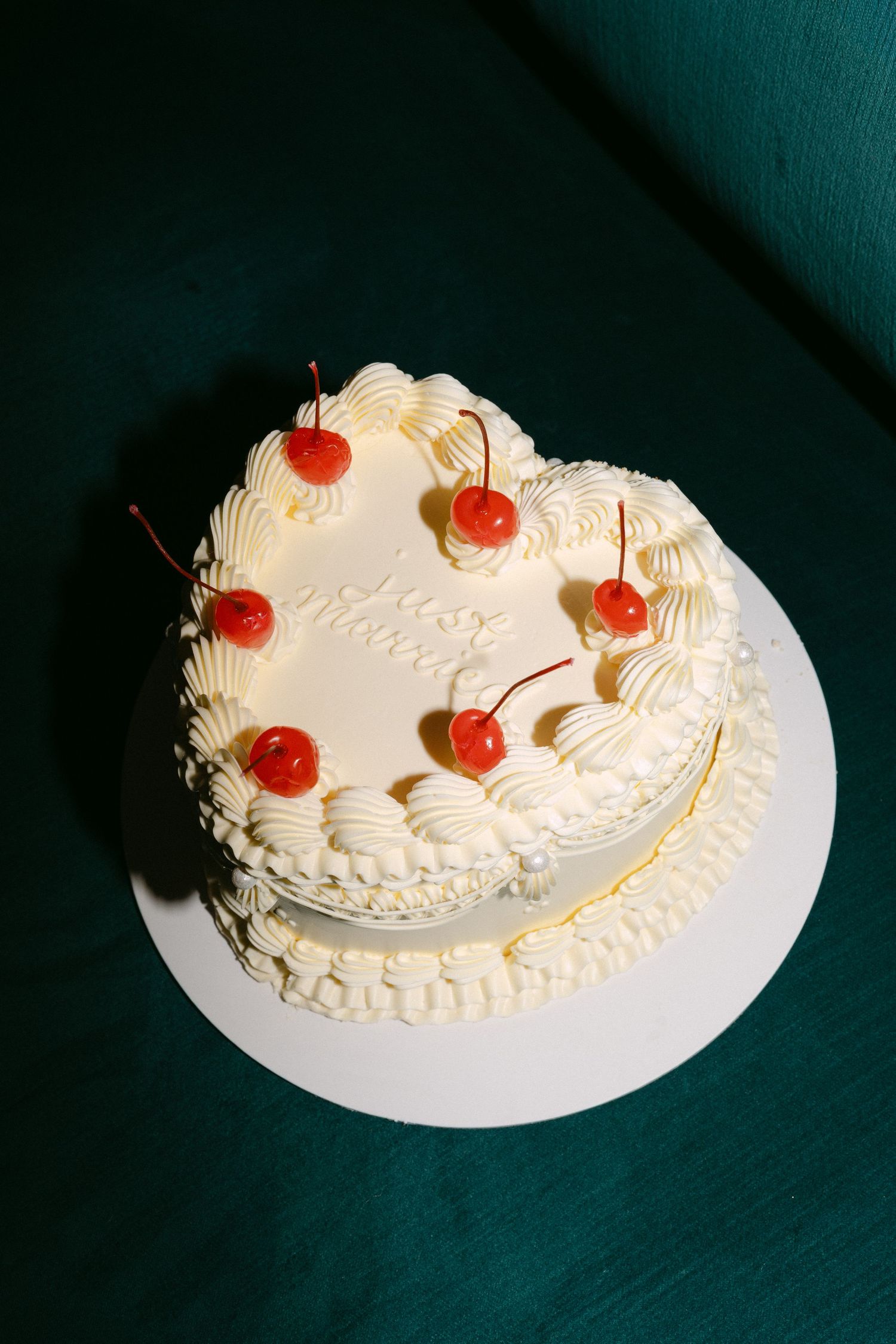 White frosted cake with red cherries arranged on top against dark background.