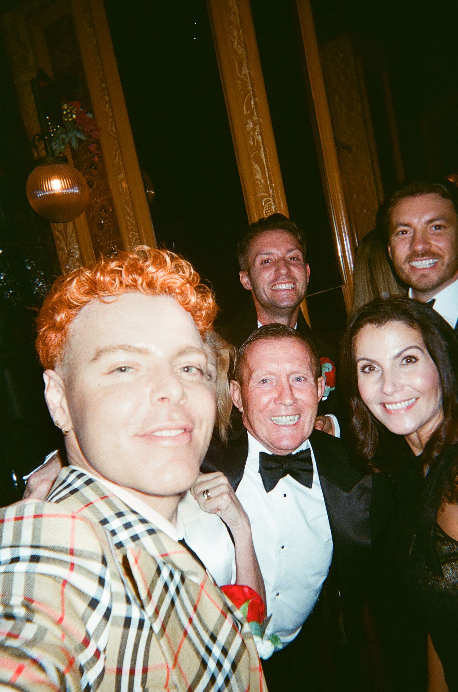 A group of formally dressed people at an evening event smiling together in a candid photo.