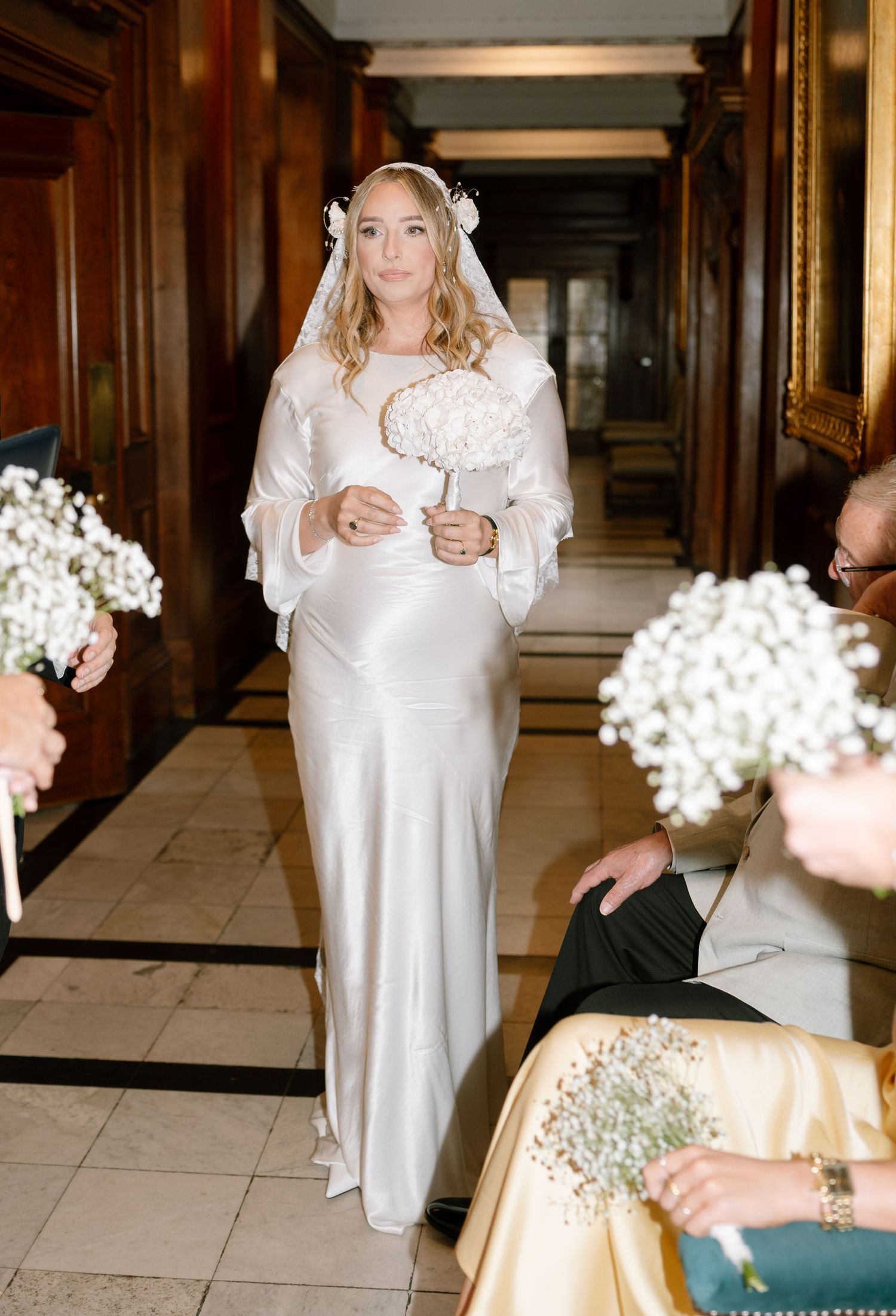 Wedding scene with white baby's breath flowers and people in formal attire standing in an elegant hallway.