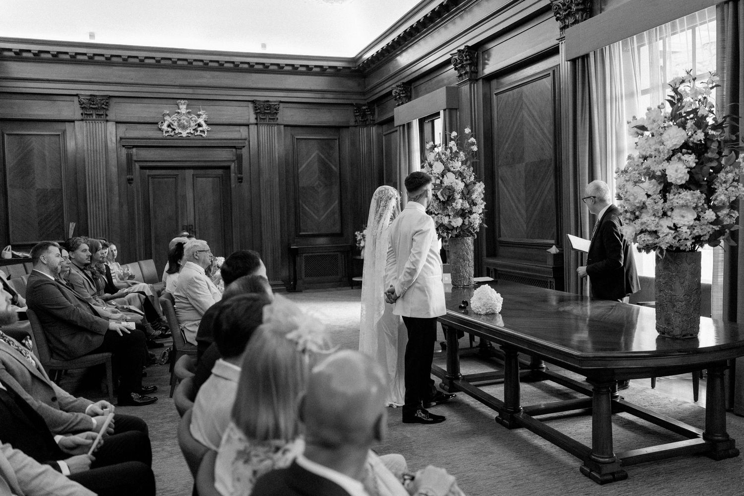 Black and white photo of wedding ceremony in wood-paneled room.