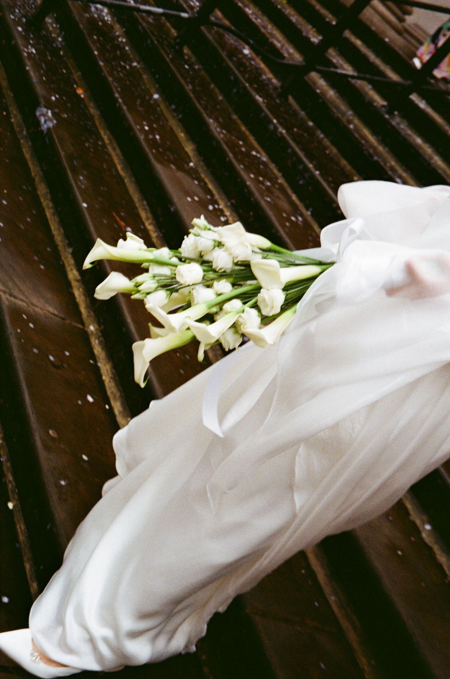 White calla lilies rest against flowing white fabric in an artistic composition.