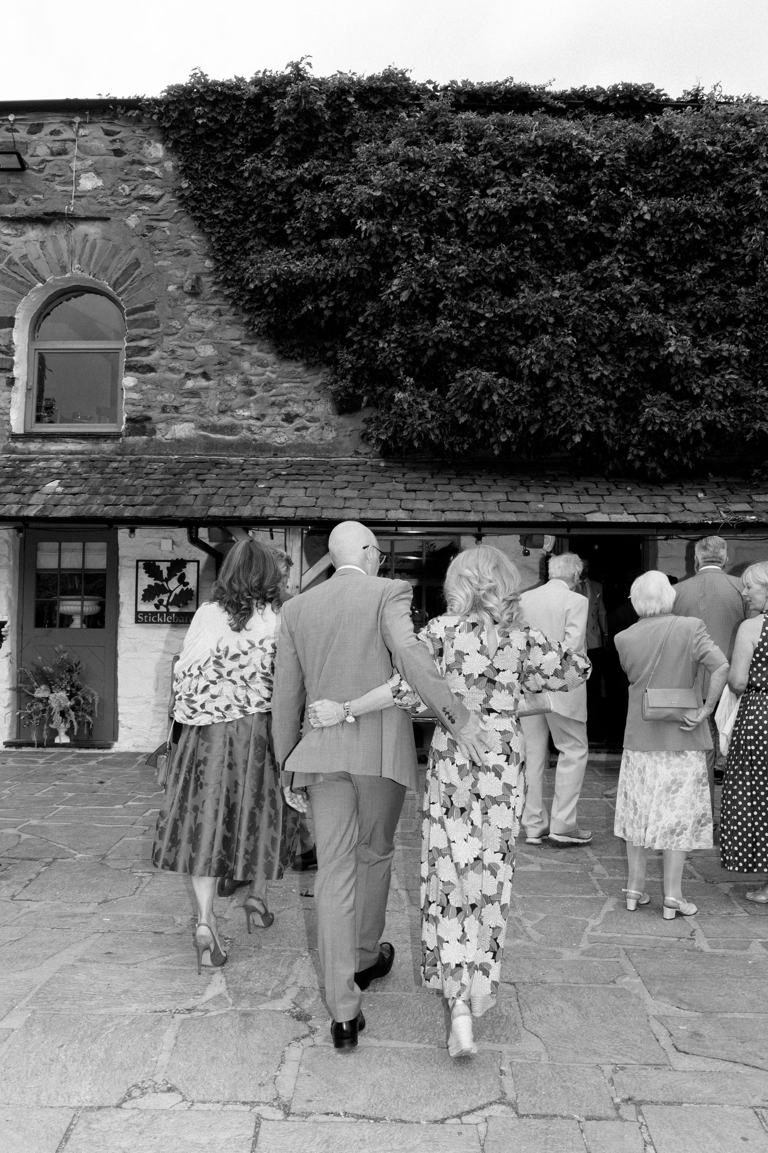 Black and white photo of wedding guests walking along a stone path.