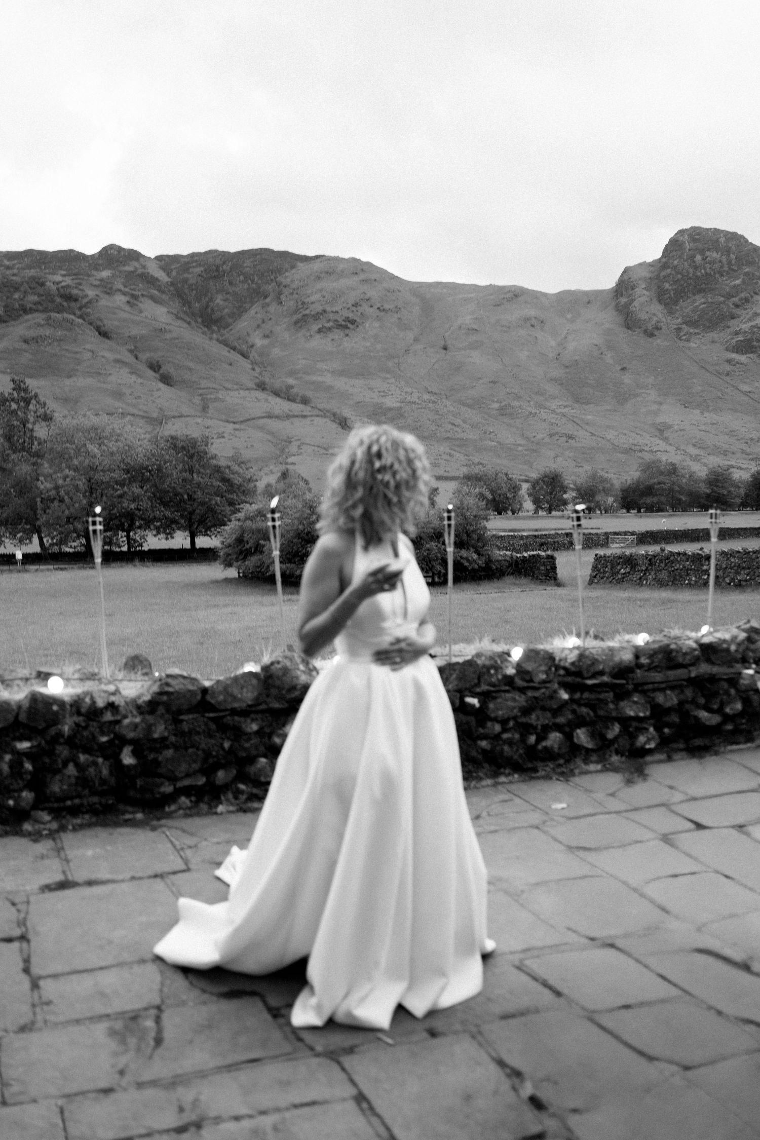 Wedding party members walk across stone patio with scenic mountain backdrop.