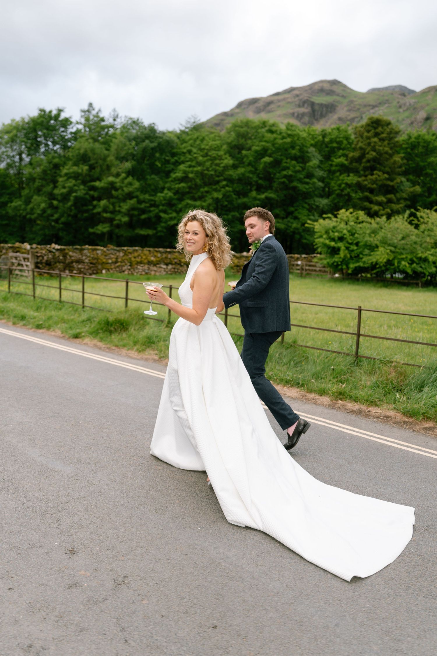Couple walking on road with flowing wedding dress in countryside setting.