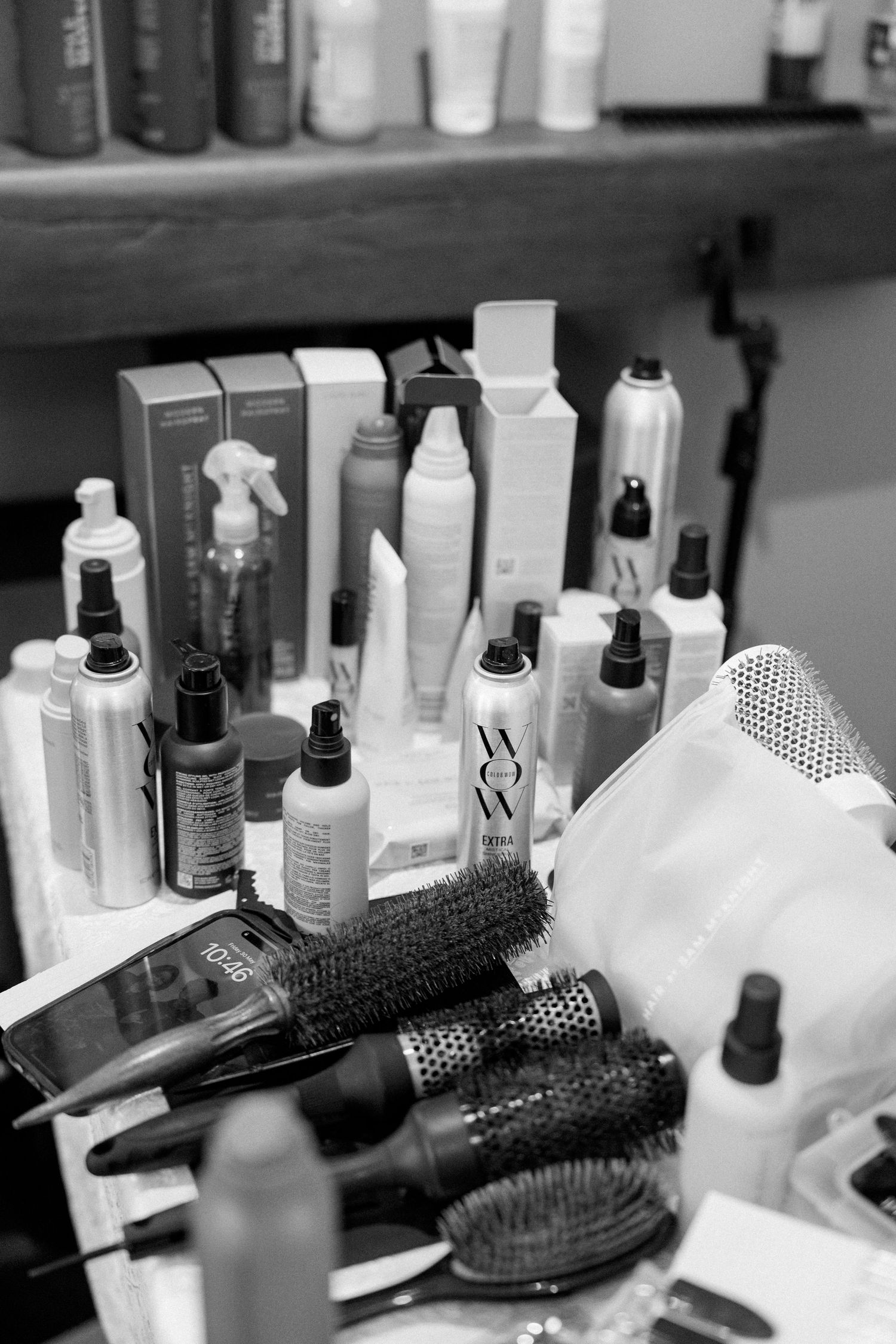 Black and white image of hair styling products and brushes arranged on a shelf.